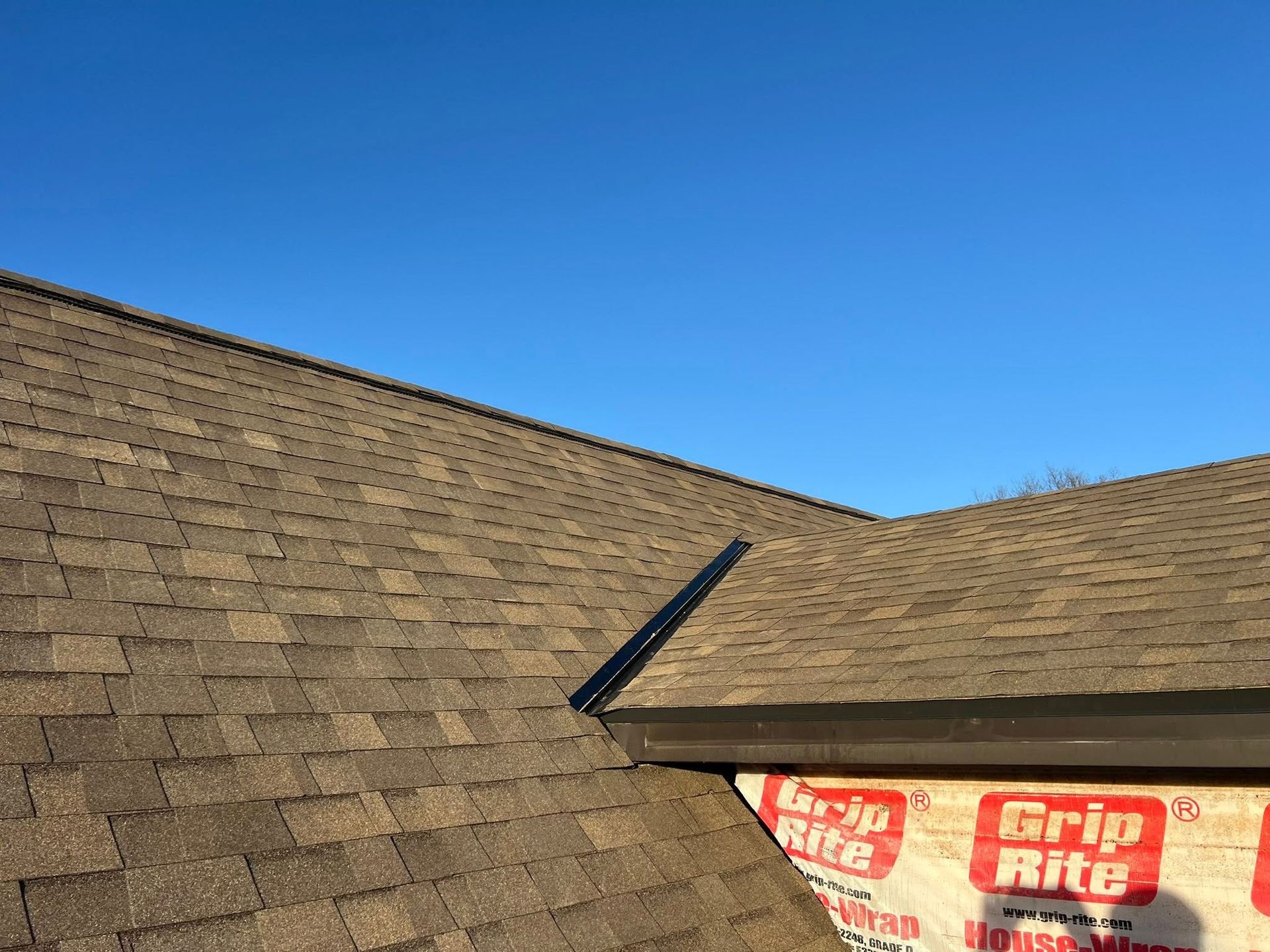 Brown shingled roof under a clear blue sky, with a rooftop vent and a small red-and-white sign near the eave