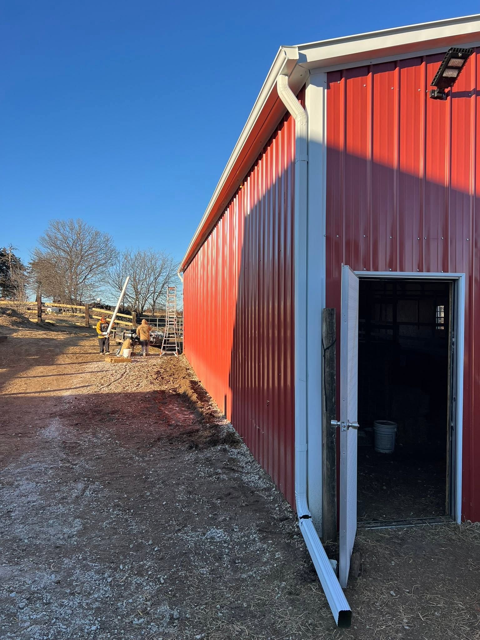 Red metal shed with open doorway on a gravel lot under a clear blue sky.