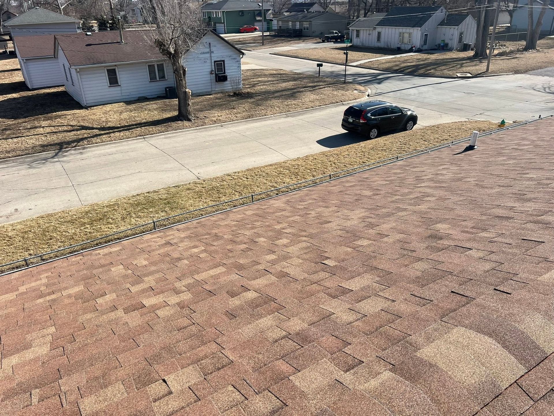 Black car on a residential street beside brick rooftops and a tree-lined neighborhood.