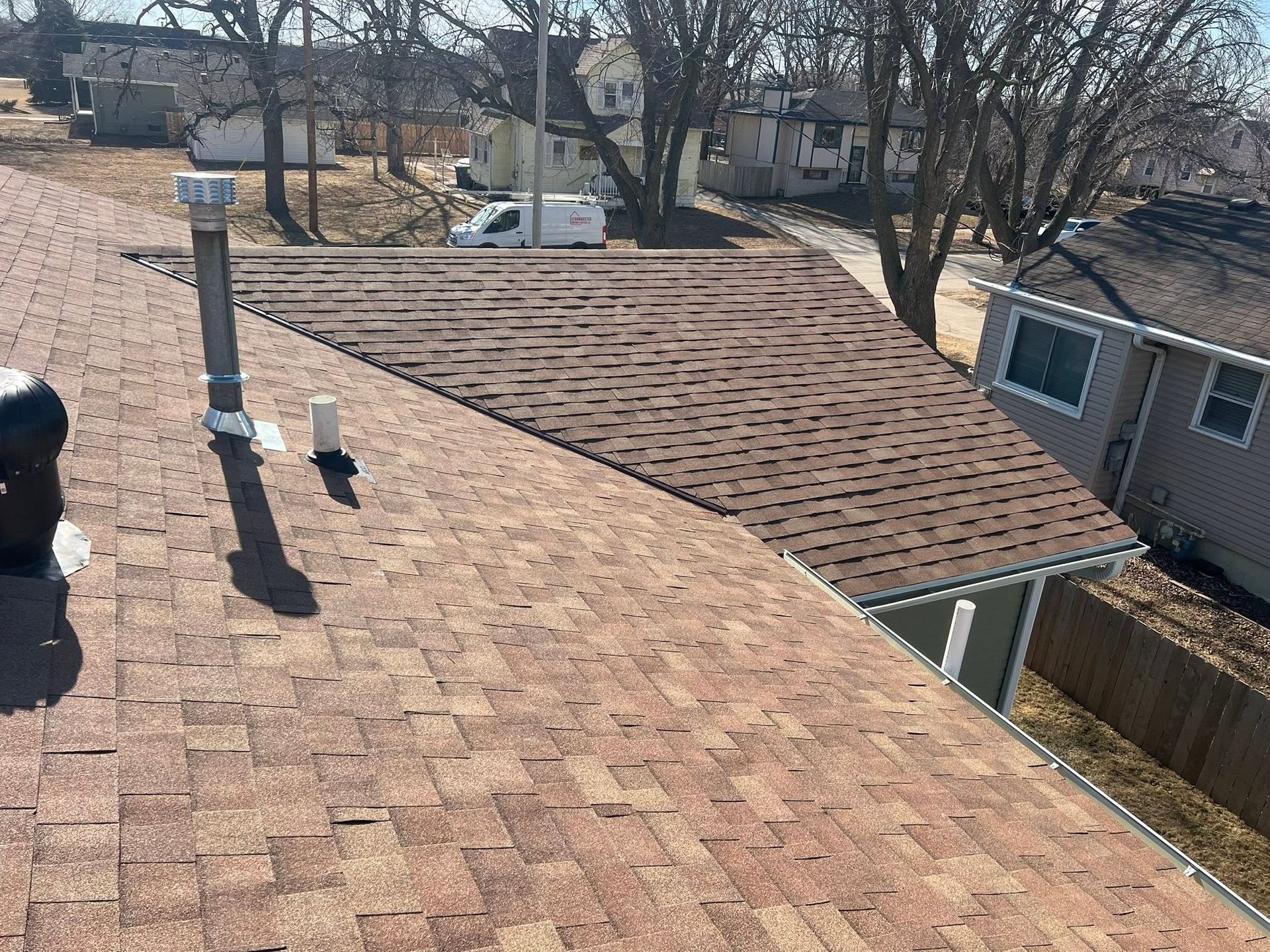 Rooftop with brown shingles, vents, and a view of leafless trees and houses in the neighborhood