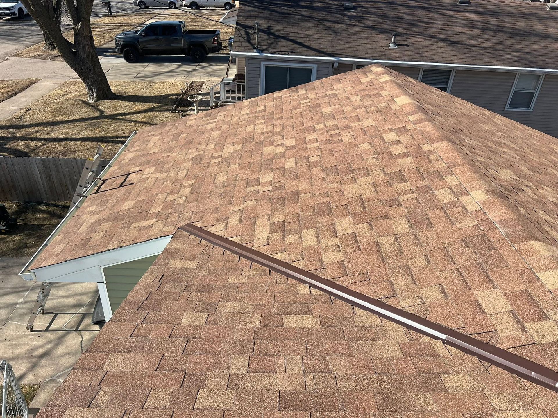 Roof with brown shingles and a skylight, viewed from above in a residential yard