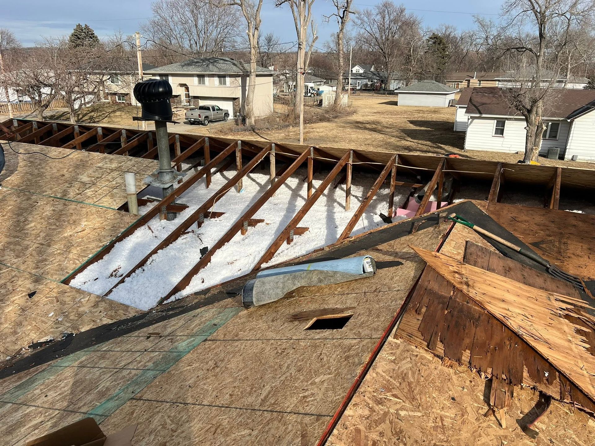 Damaged roof with exposed rafters and torn shingles in a residential area.
