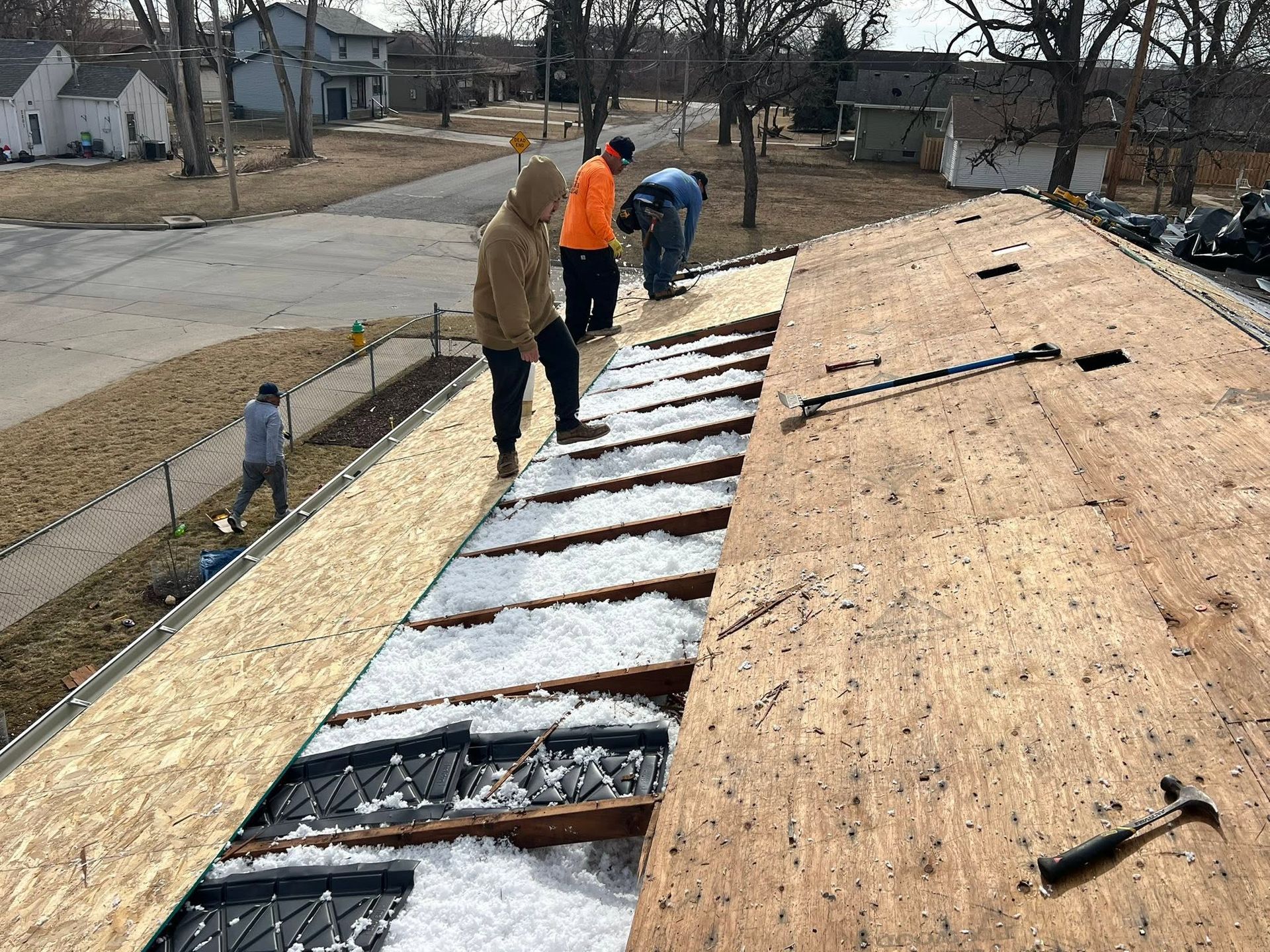 Workers installing roof sheathing, with foam board insulation visible along one side