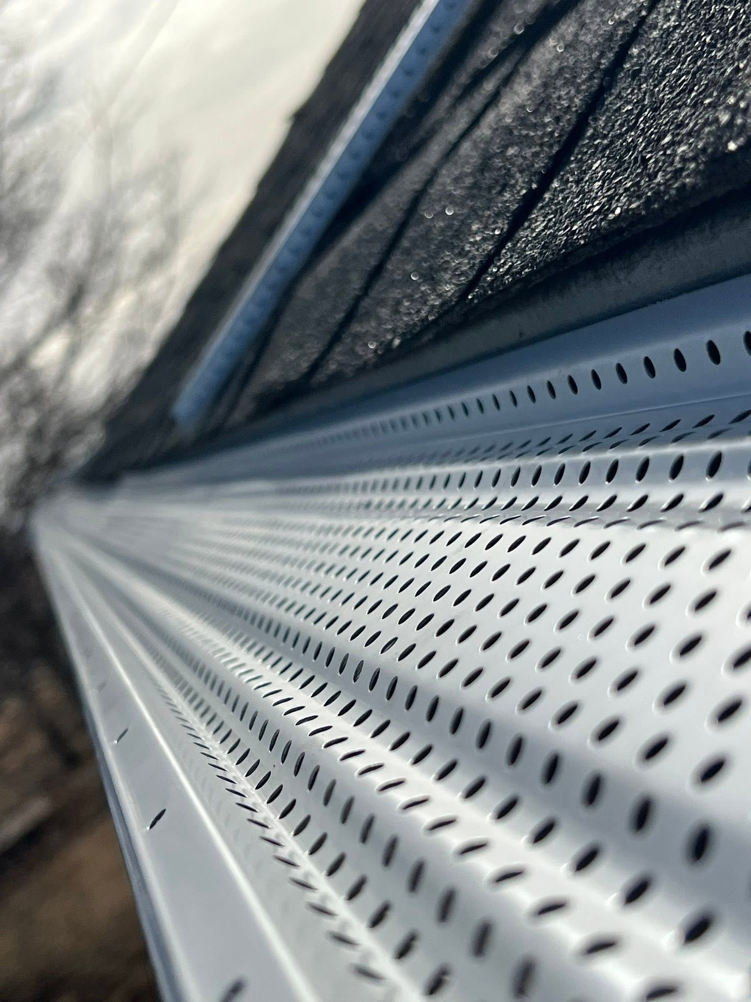 Close-up of a white perforated metal siding with a dark window frame and outdoor reflections