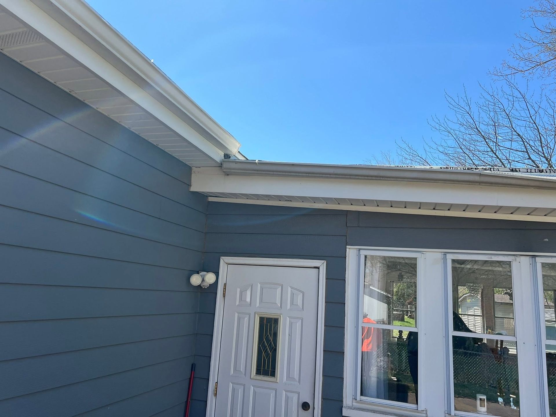 Side view of a gray house exterior with a white door and windows under a blue sky.