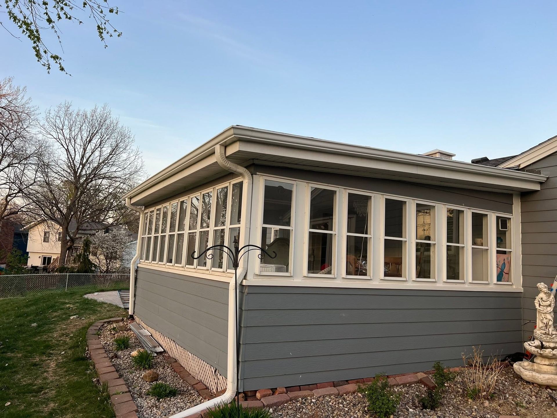 Gray enclosed porch with many windows on a house, next to a stone fountain and garden path