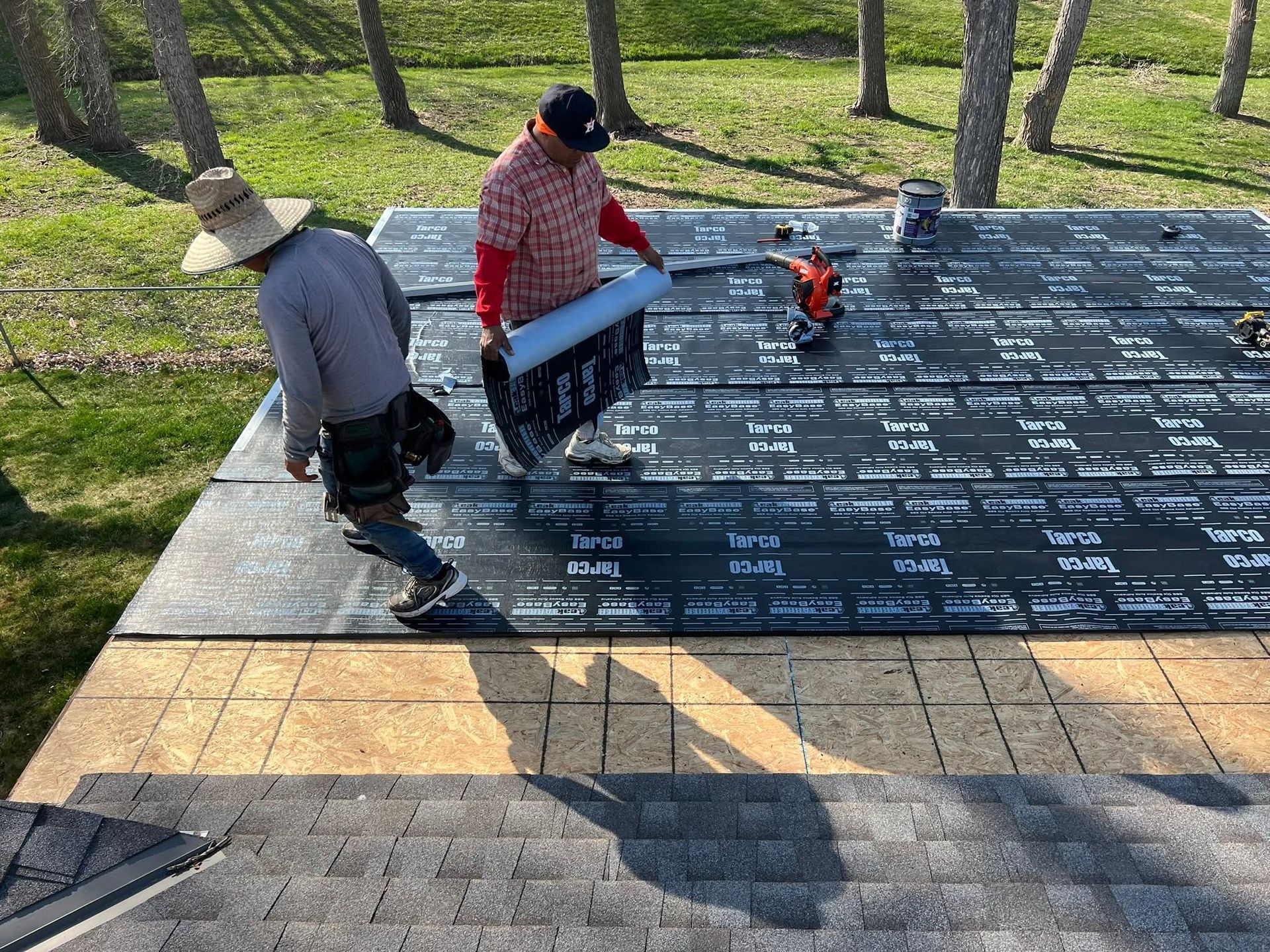 Two workers installing a dark memorial plaque on a stone platform in a park.