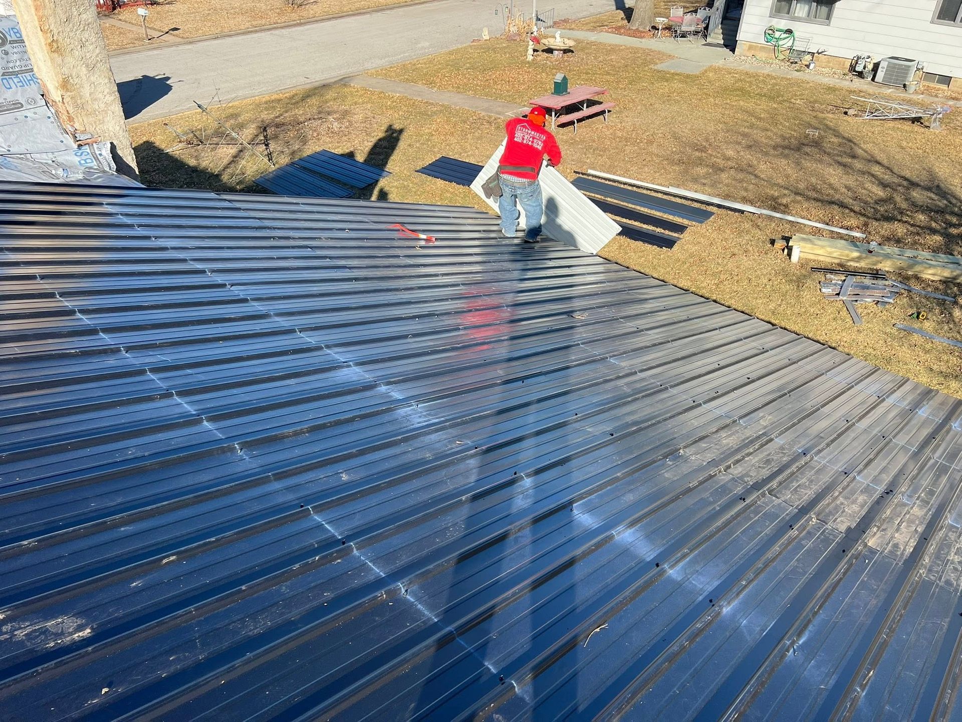 Worker in red shirt installing a shiny corrugated metal roof on a house frame