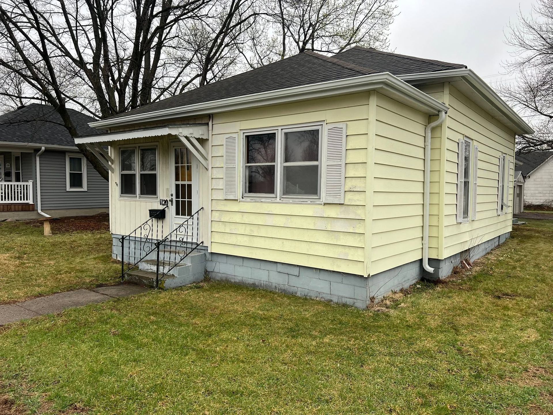 Small yellow single-story house with a front porch and gray foundation on a grassy lot