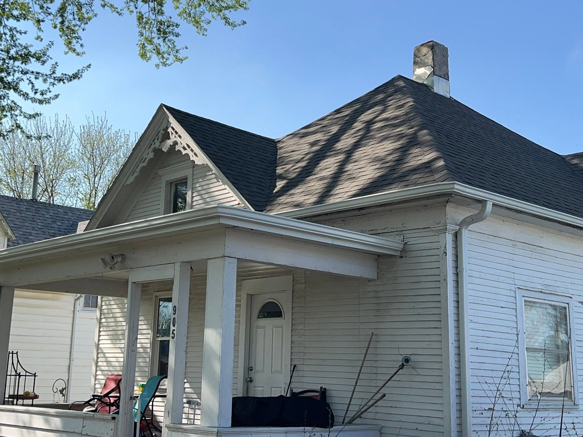 White house with a covered porch, dark shingled roof, and chimney under a clear sky
