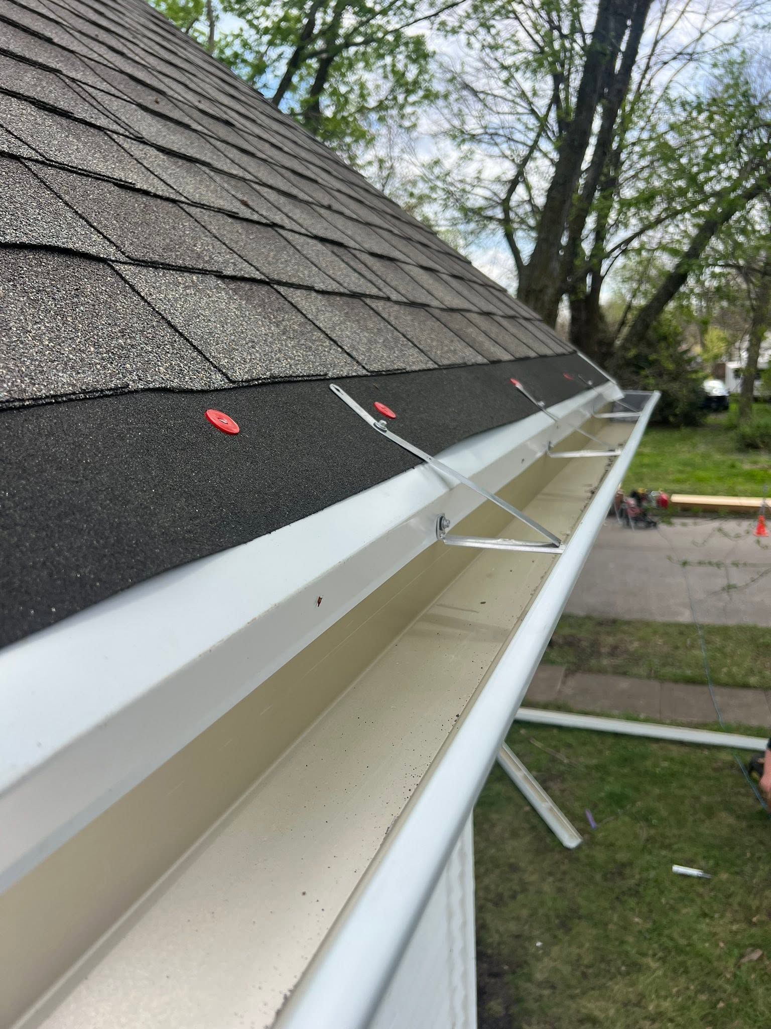White gutters along a shingled roof with a downspout, viewed from the eaves side outdoors.
