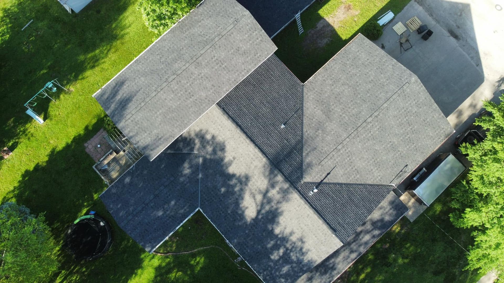 Aerial view of a gray-roofed house surrounded by green trees and lawn.