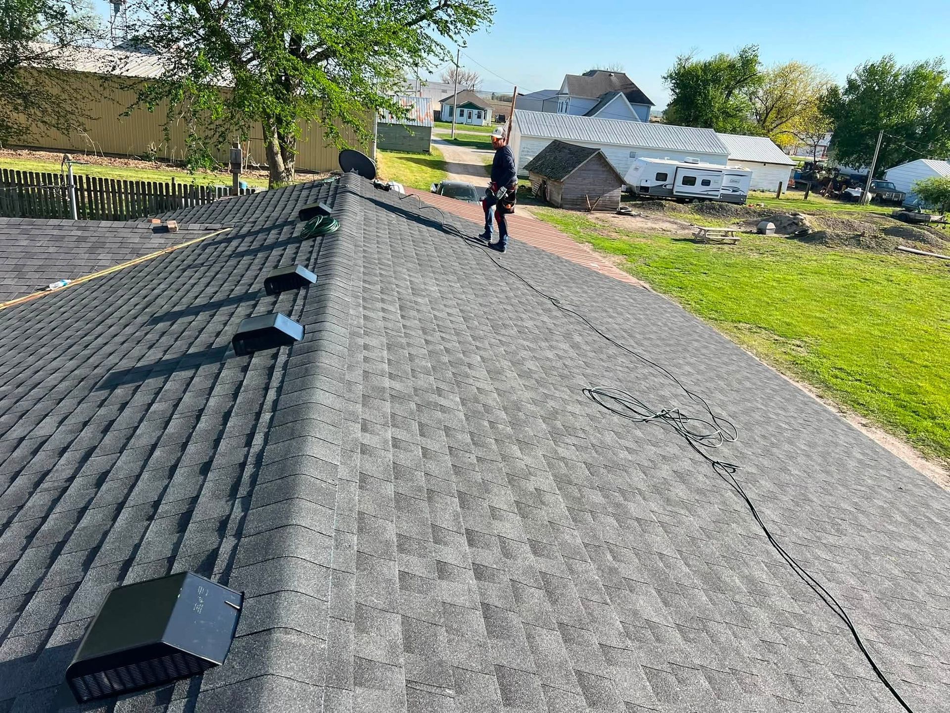Solar panel array on a roof with a worker standing on it beside a grassy yard and houses