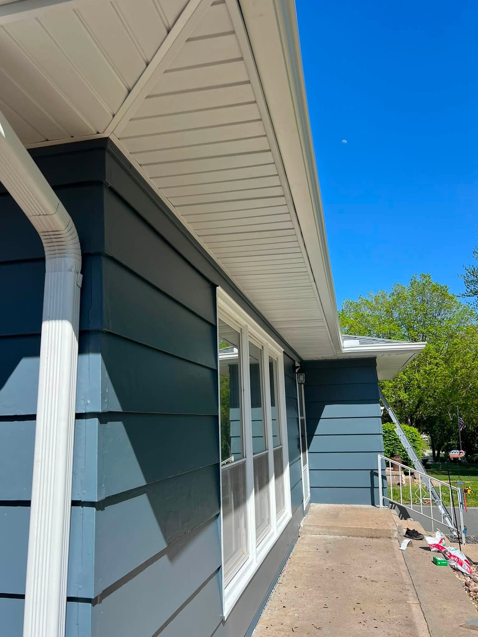 Blue house exterior with white trim, sliding glass doors, and a sunlit side walkway under a clear sky