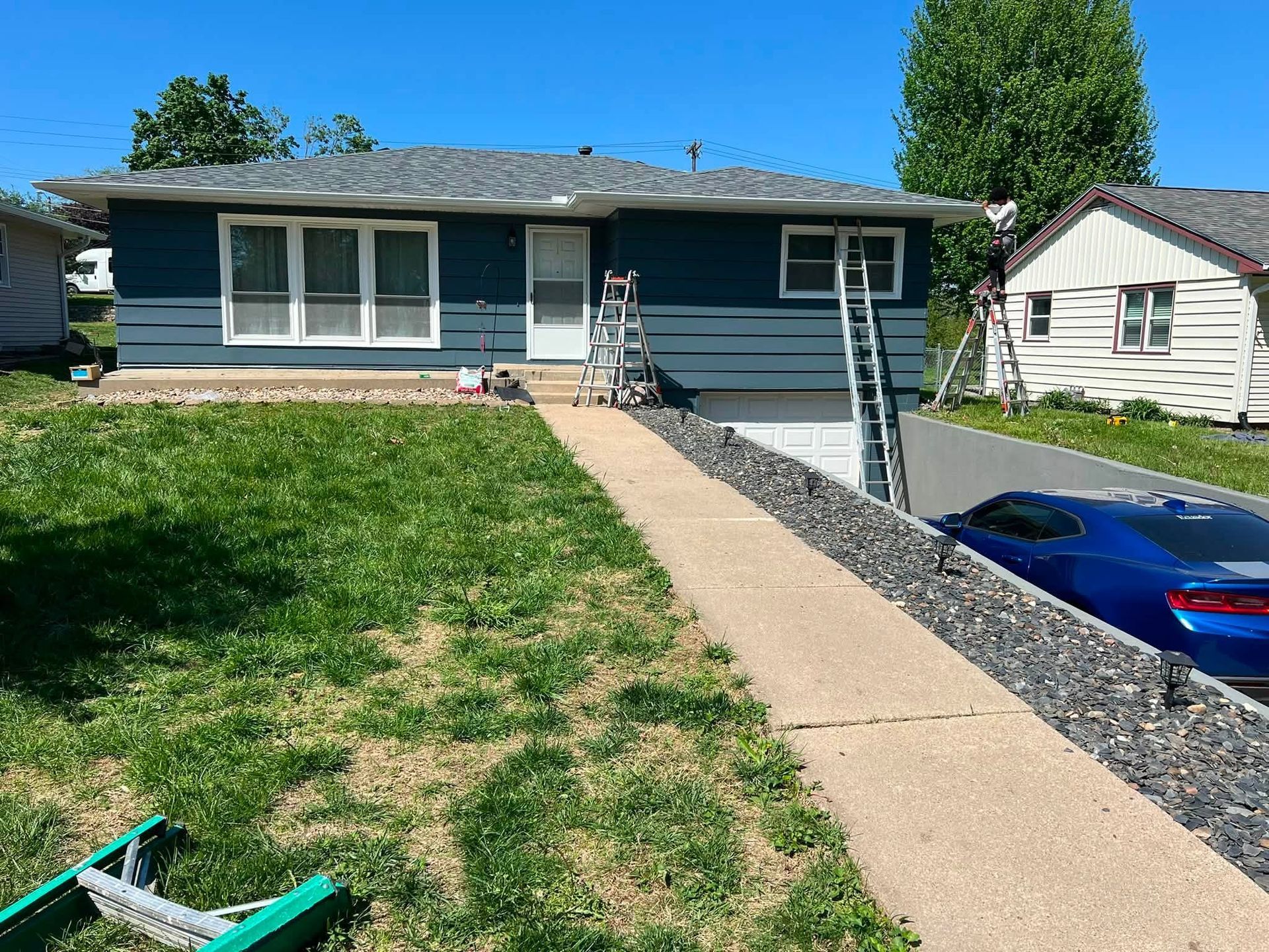 Single-story blue house with a front ramp, sloped walkway, and a car parked below on the right.