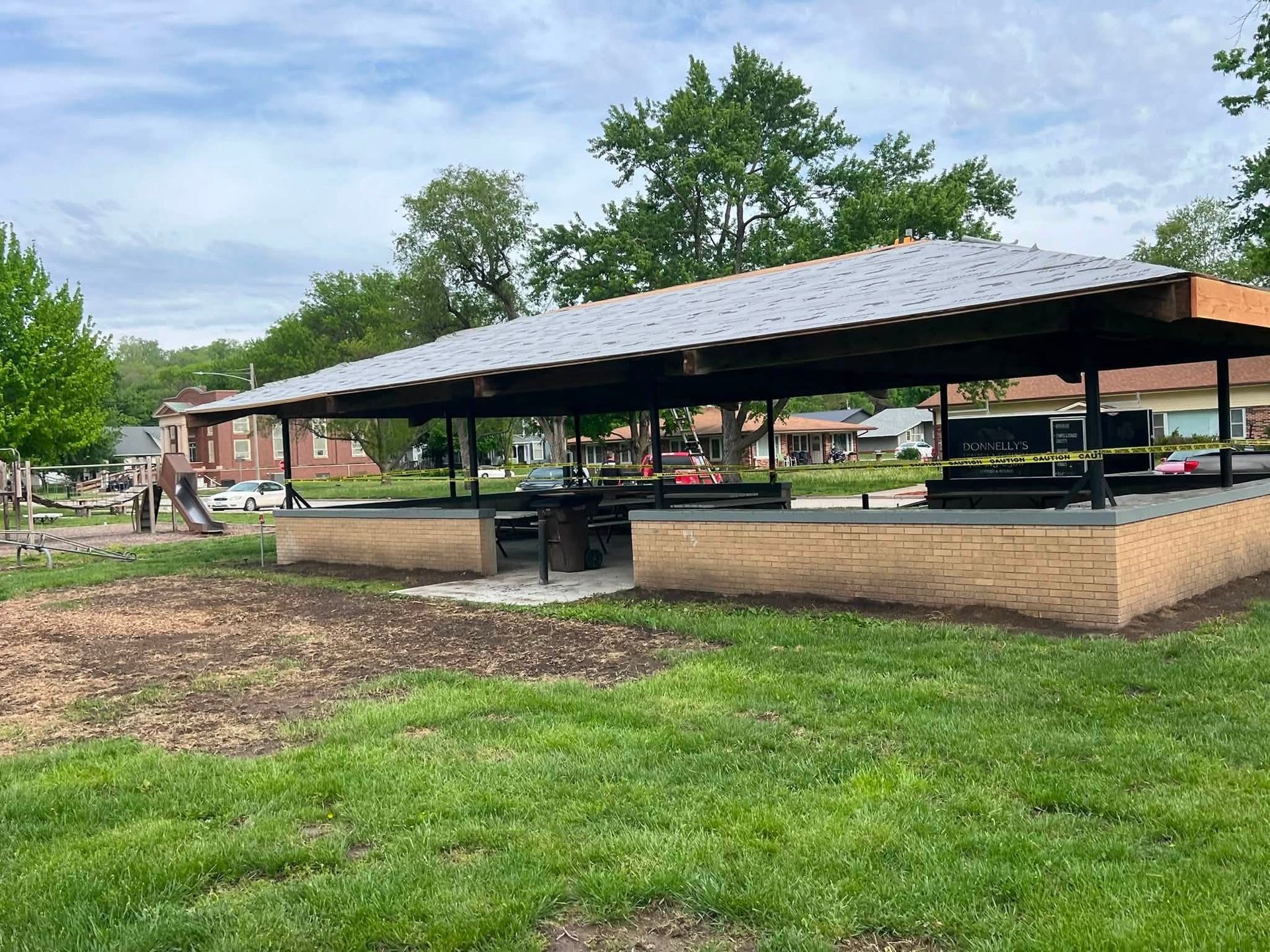 Covered park pavilion with picnic tables and benches on a grassy lawn under a cloudy sky