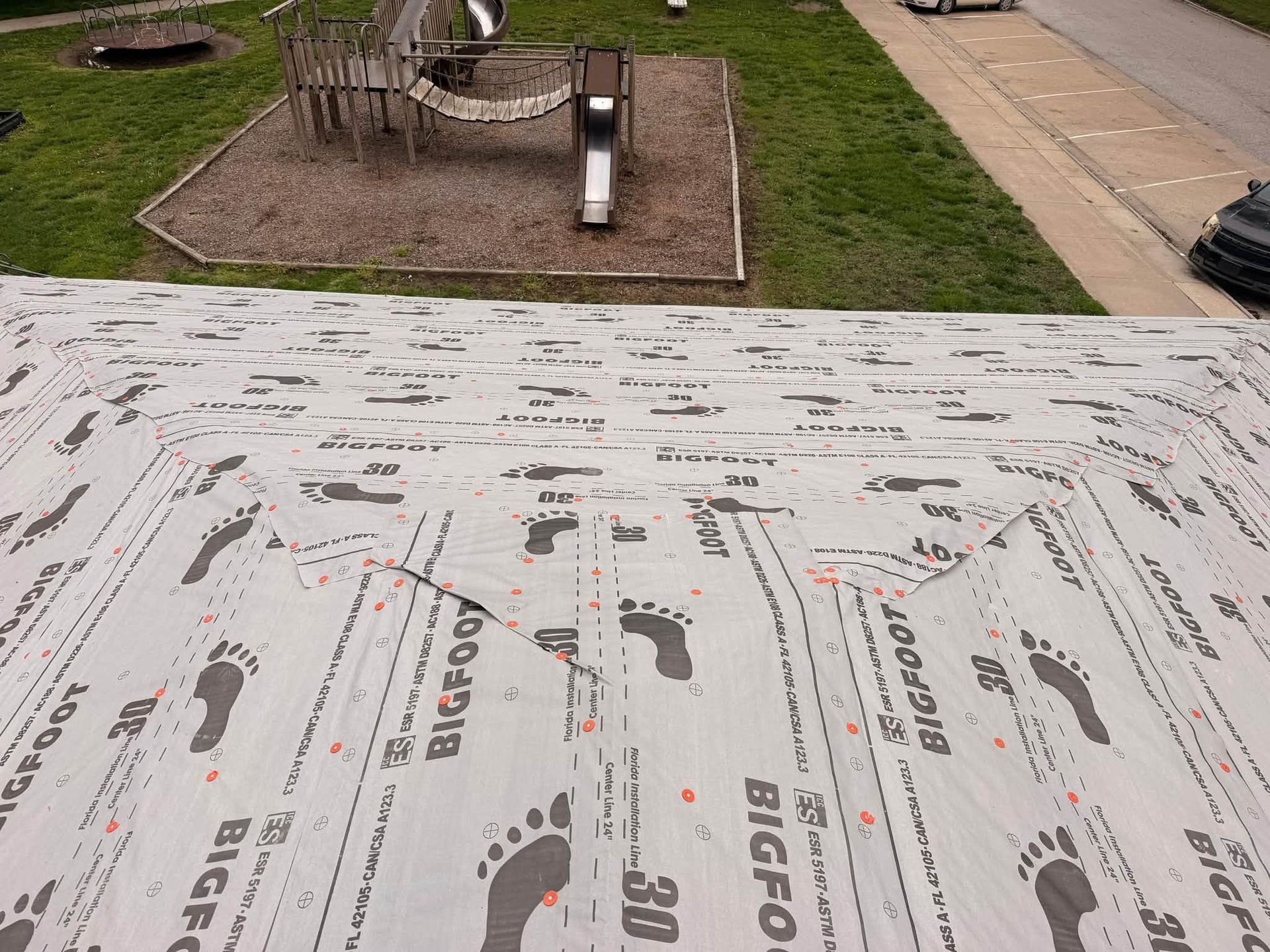 Roof underlayment with printed logos, overlooking a backyard playground and a patio.
