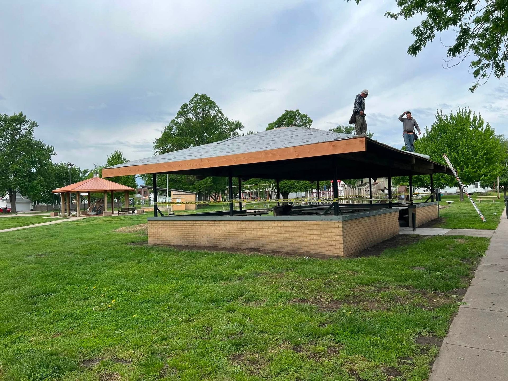 Open-air pavilion with orange roof in a grassy park beside a sidewalk