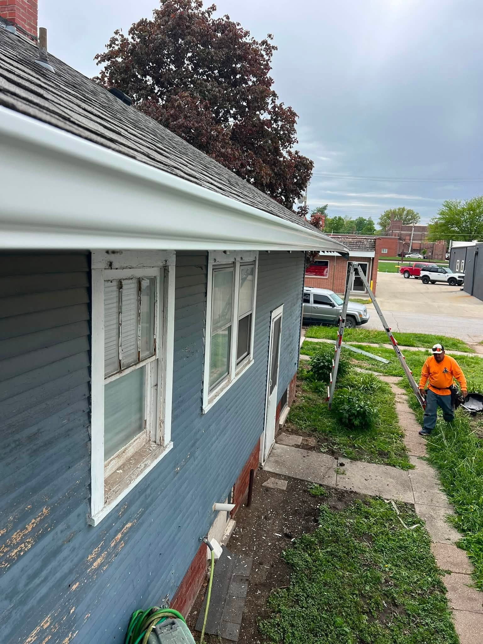 Blue house exterior with white-trimmed windows and a worker in an orange jacket near the side yard