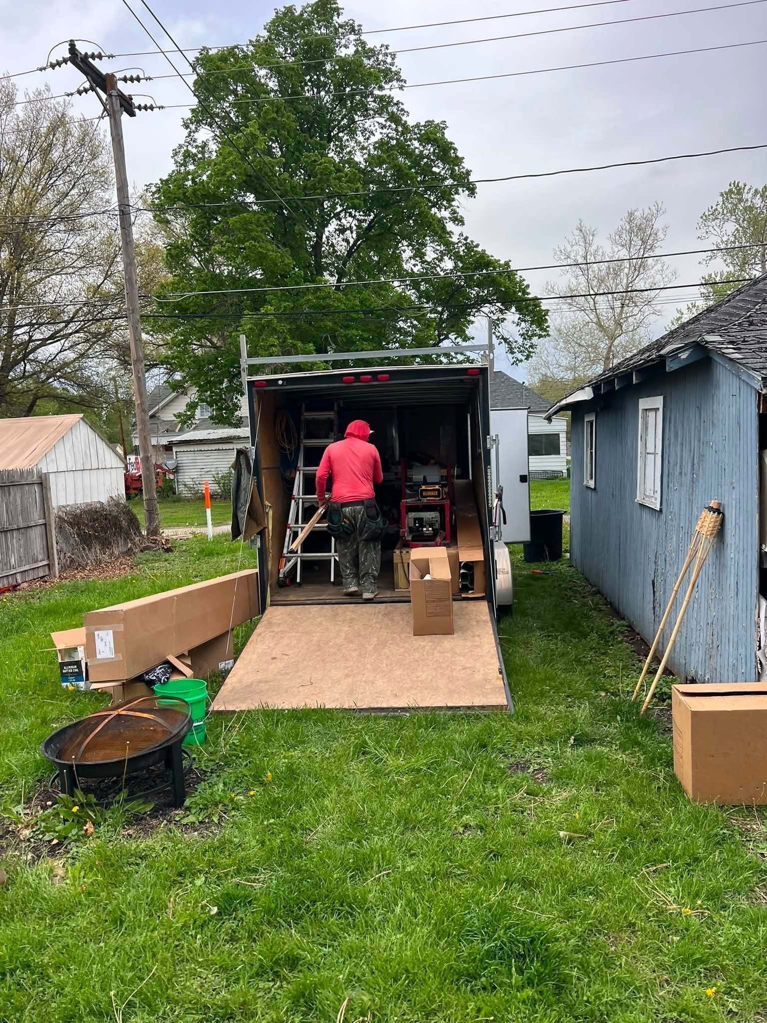 Person in pink shirt working inside open moving truck in a backyard between sheds.