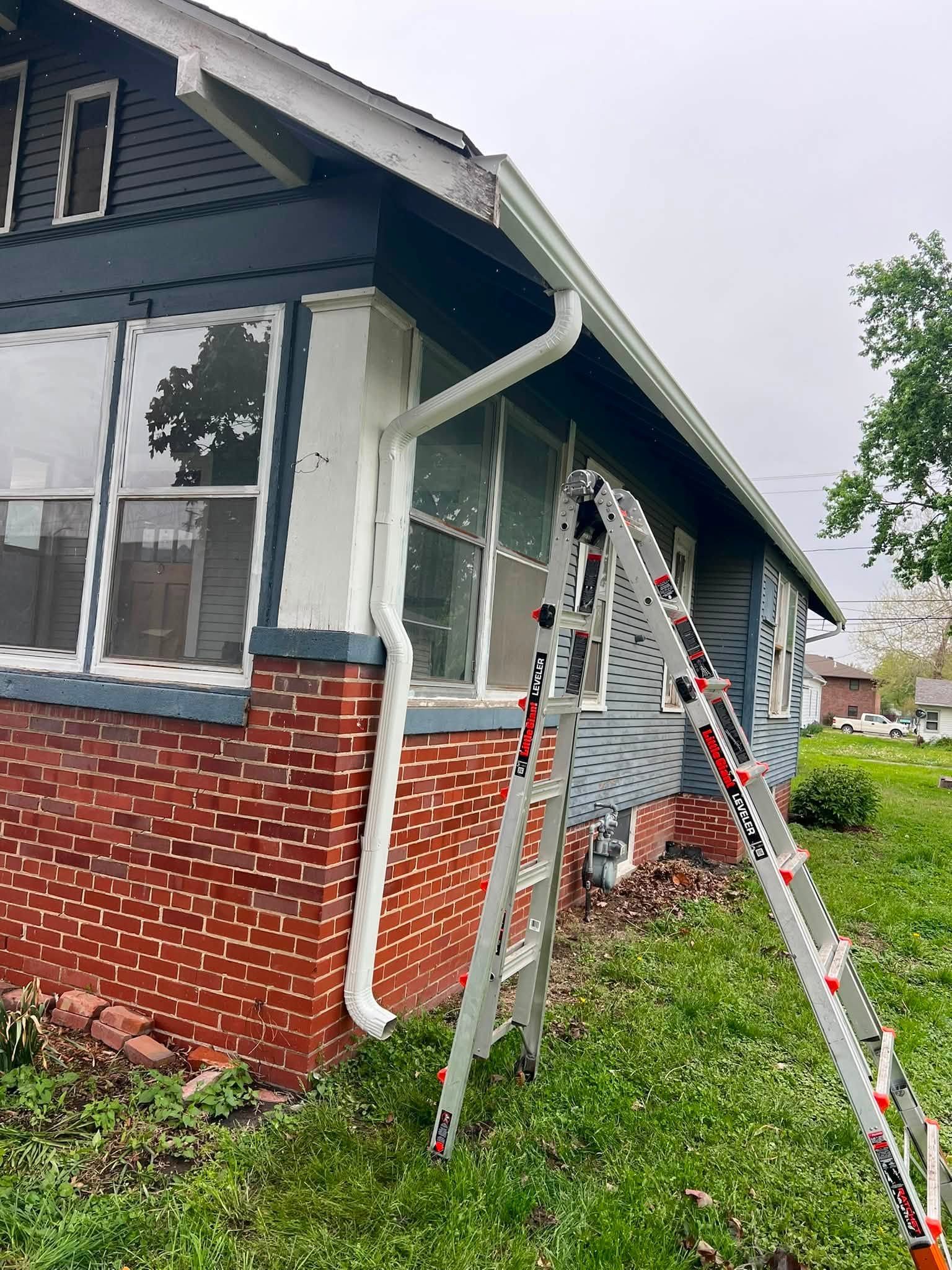 House exterior with brick porch, large windows, and two ladders leaning against the front in a grassy yard