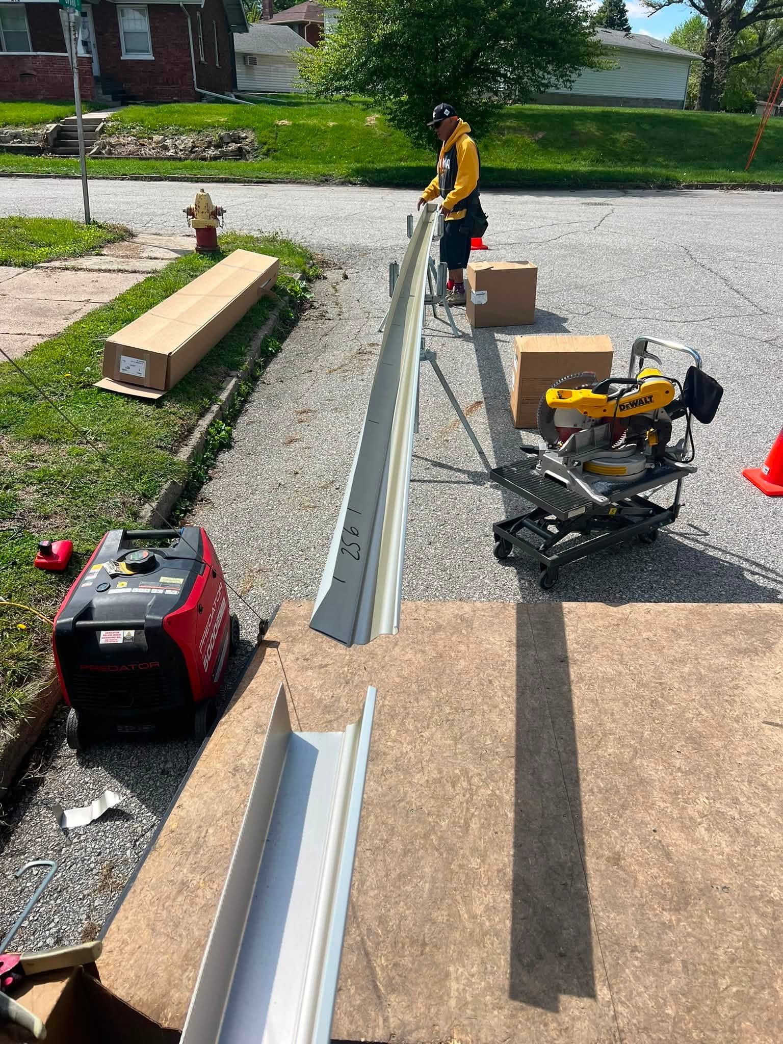 Workers installing long metal gutter sections along a gravel driveway with tools and boxes nearby