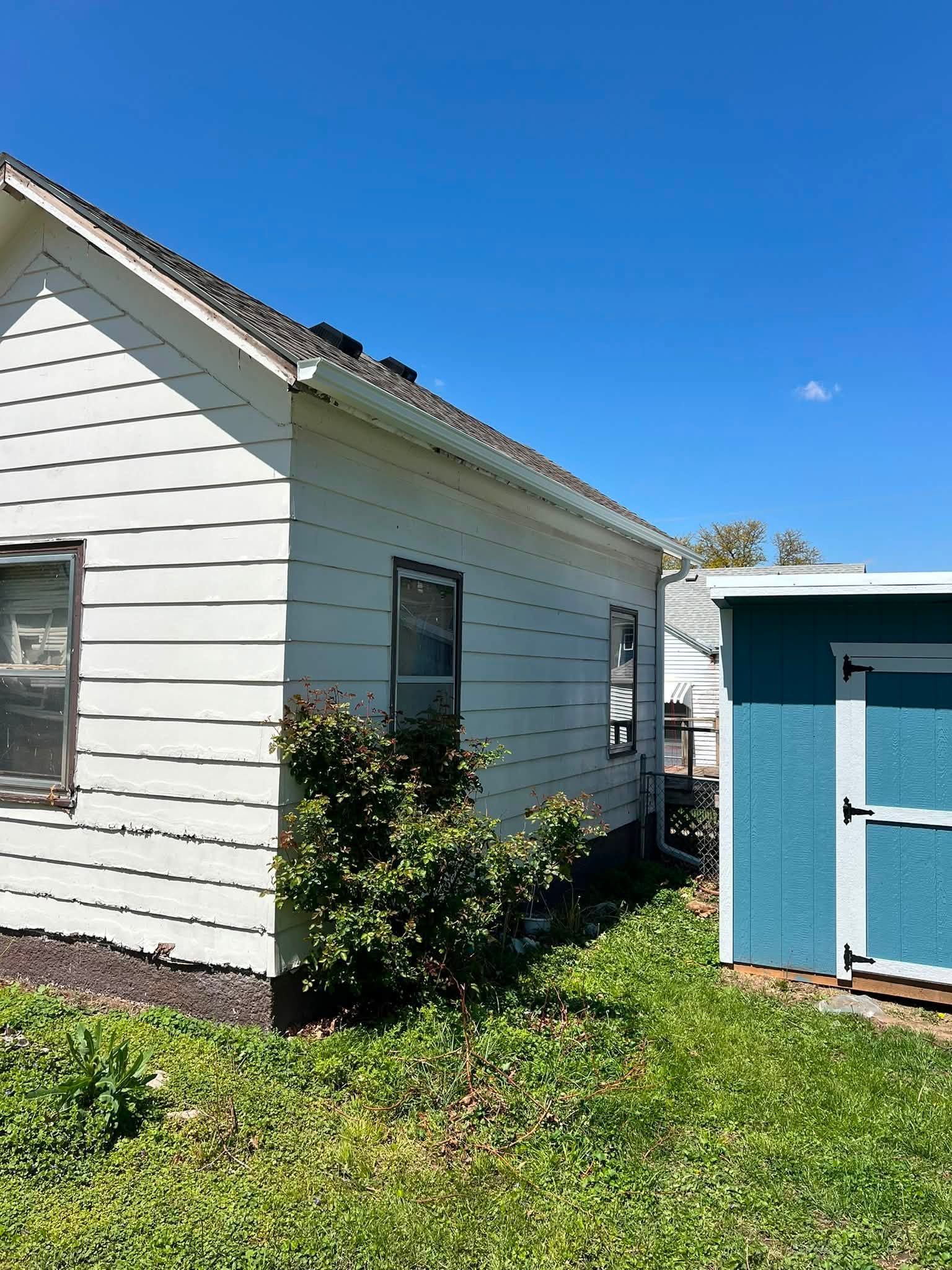 White house siding beside a small blue shed on a sunny grassy yard