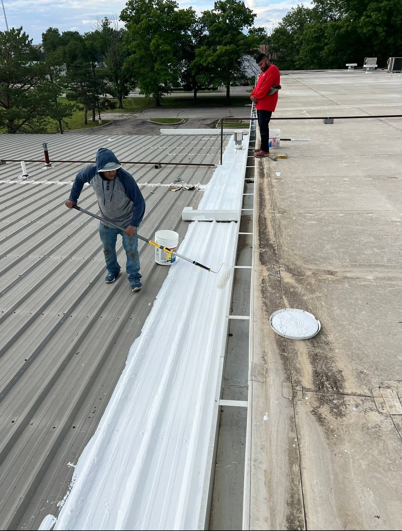 Two workers on a rooftop installing white metal panels beside a gray roof edge