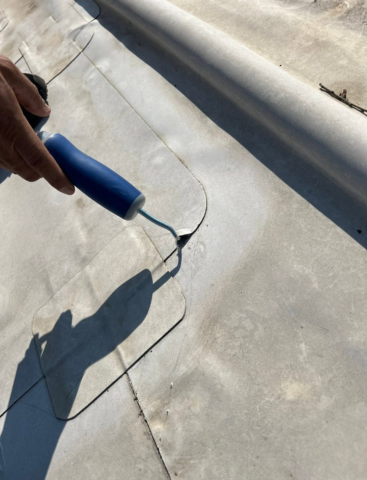 Hand using a blue tool to patch a crack in a gray concrete surface outdoors