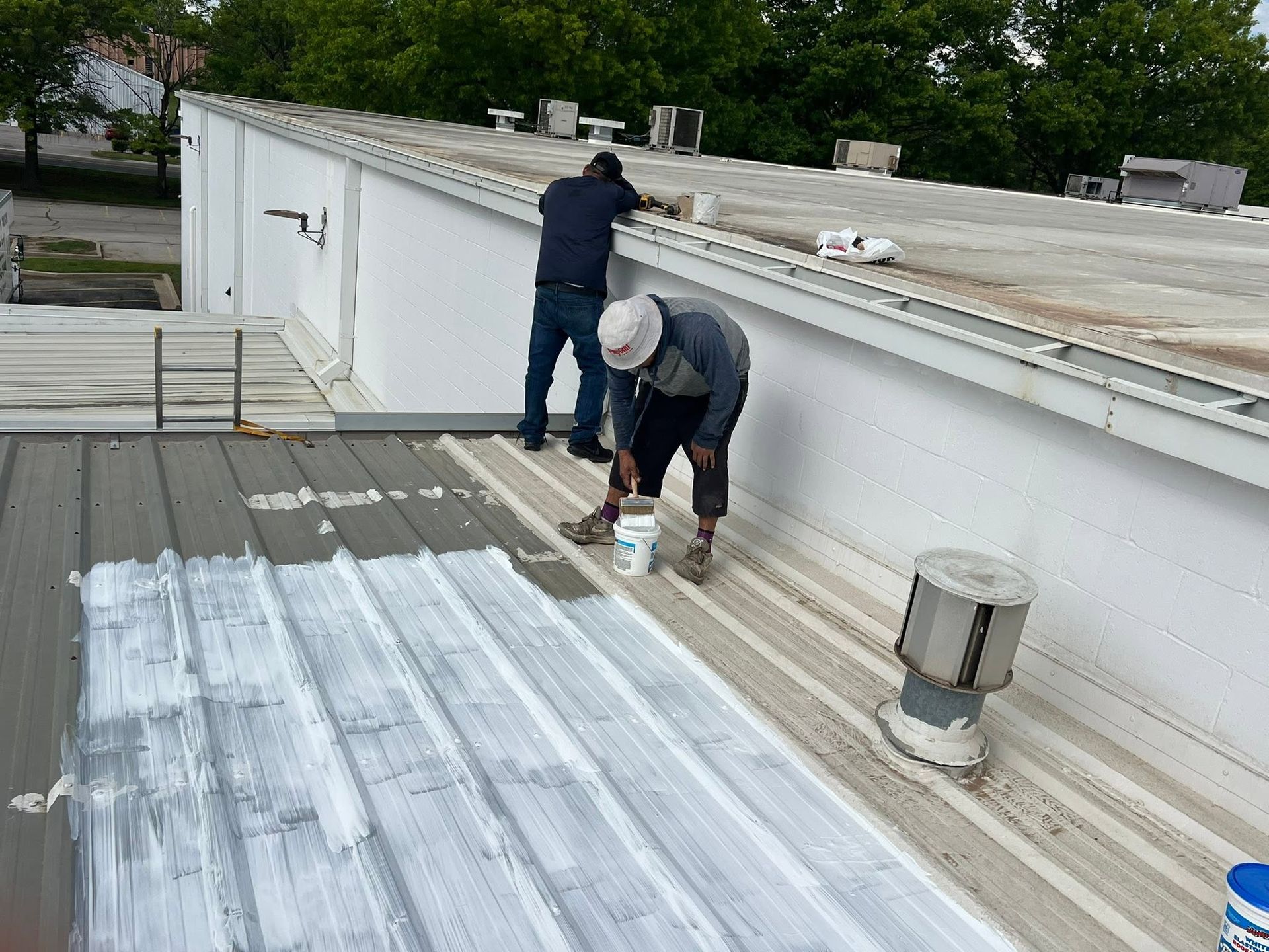 Two workers on a rooftop inspecting a white roof near a large vent