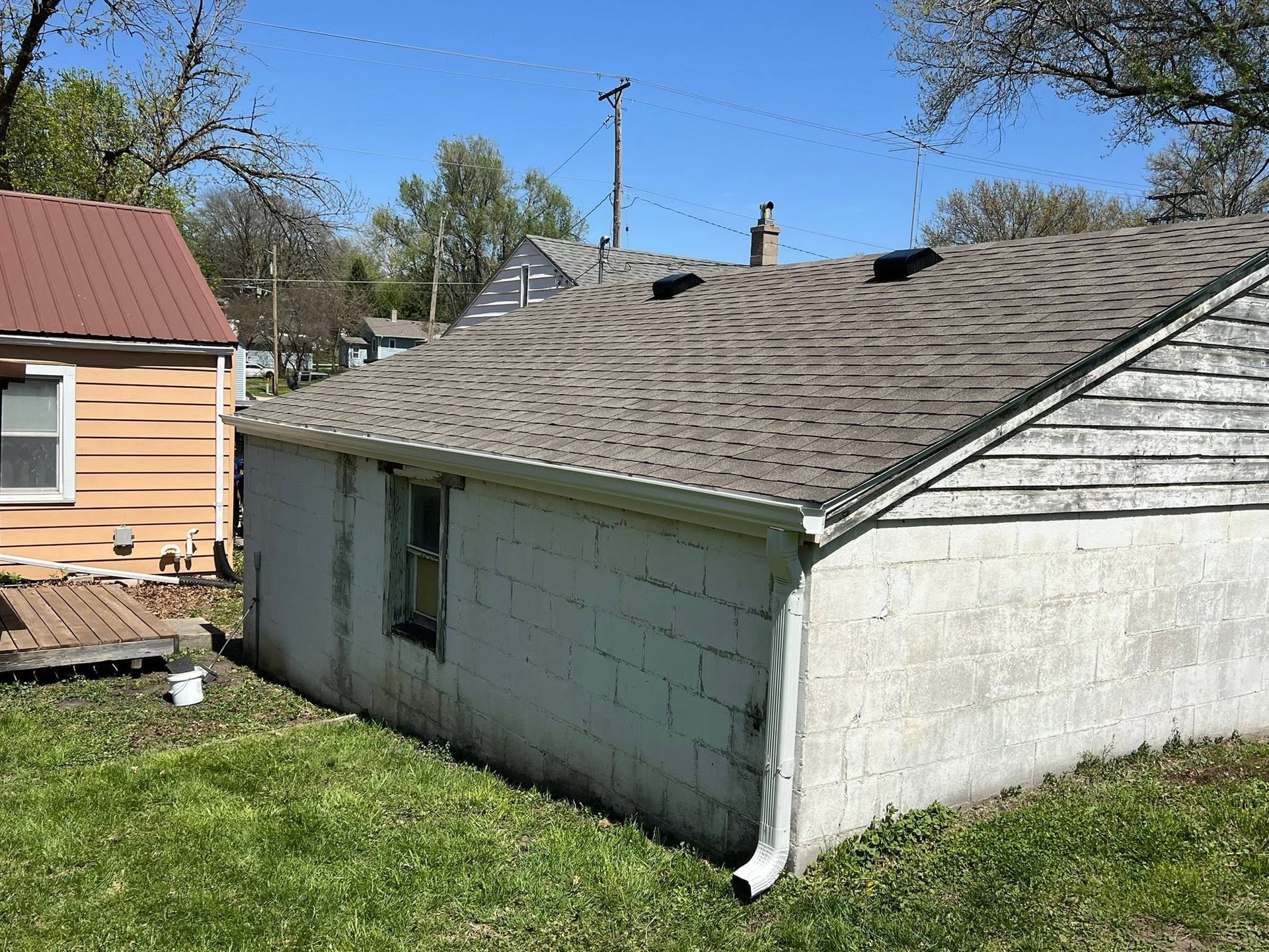 Small white cinderblock garage with a shingled roof beside a peach house on a grassy yard.