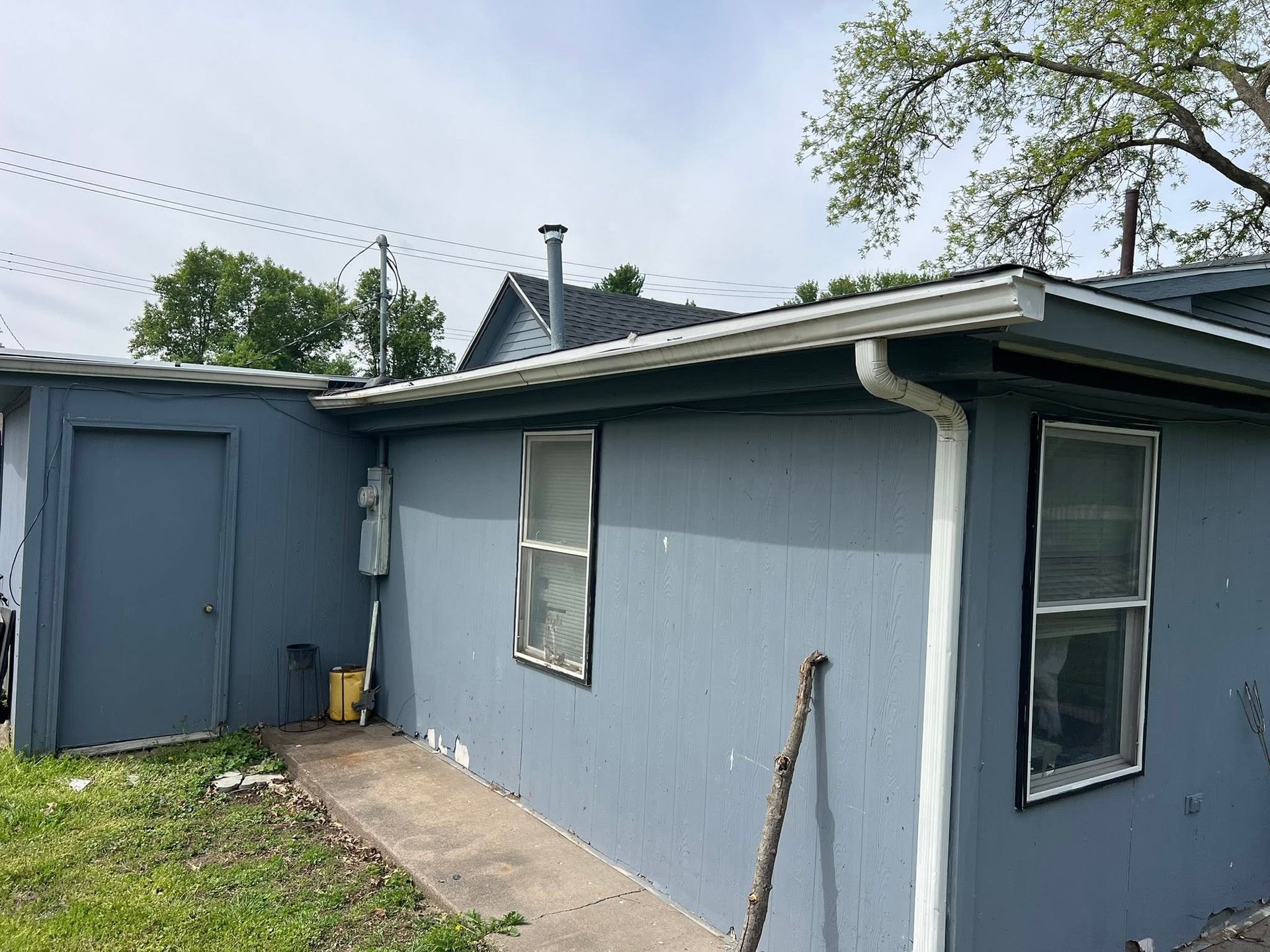 Blue-gray house exterior with a side door, windows, and a concrete walkway beside a grassy yard