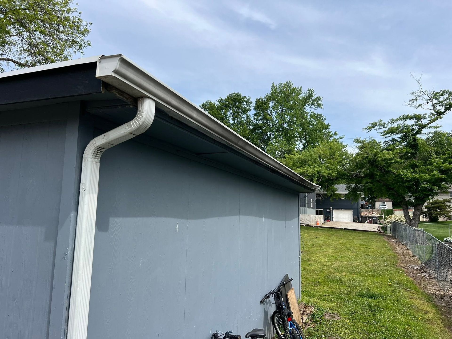 Gray building exterior with a white gutter, grassy yard, and a ladder leaning against the wall