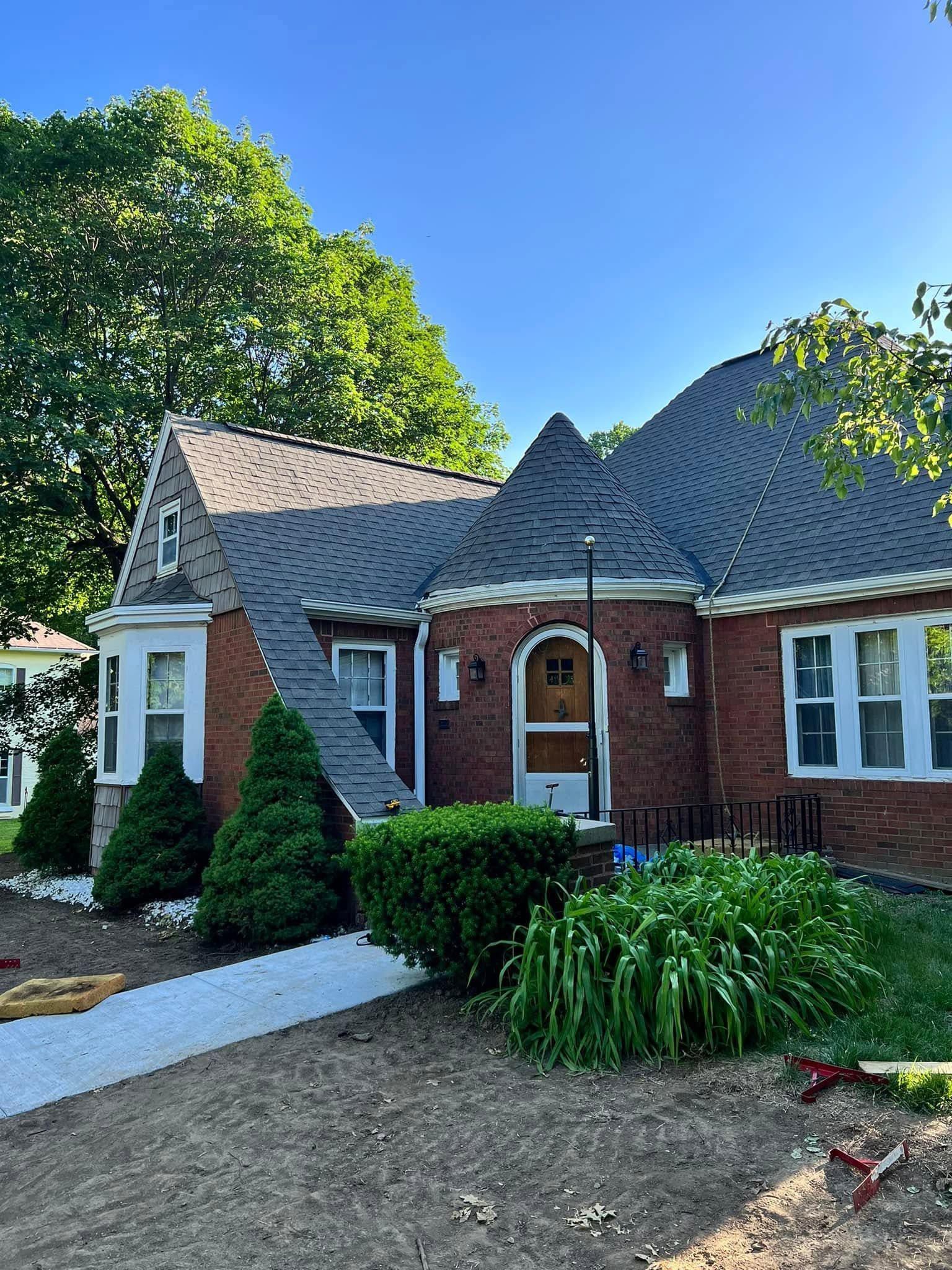 Brick house with white trim, arched front door, and manicured shrubs under a clear blue sky