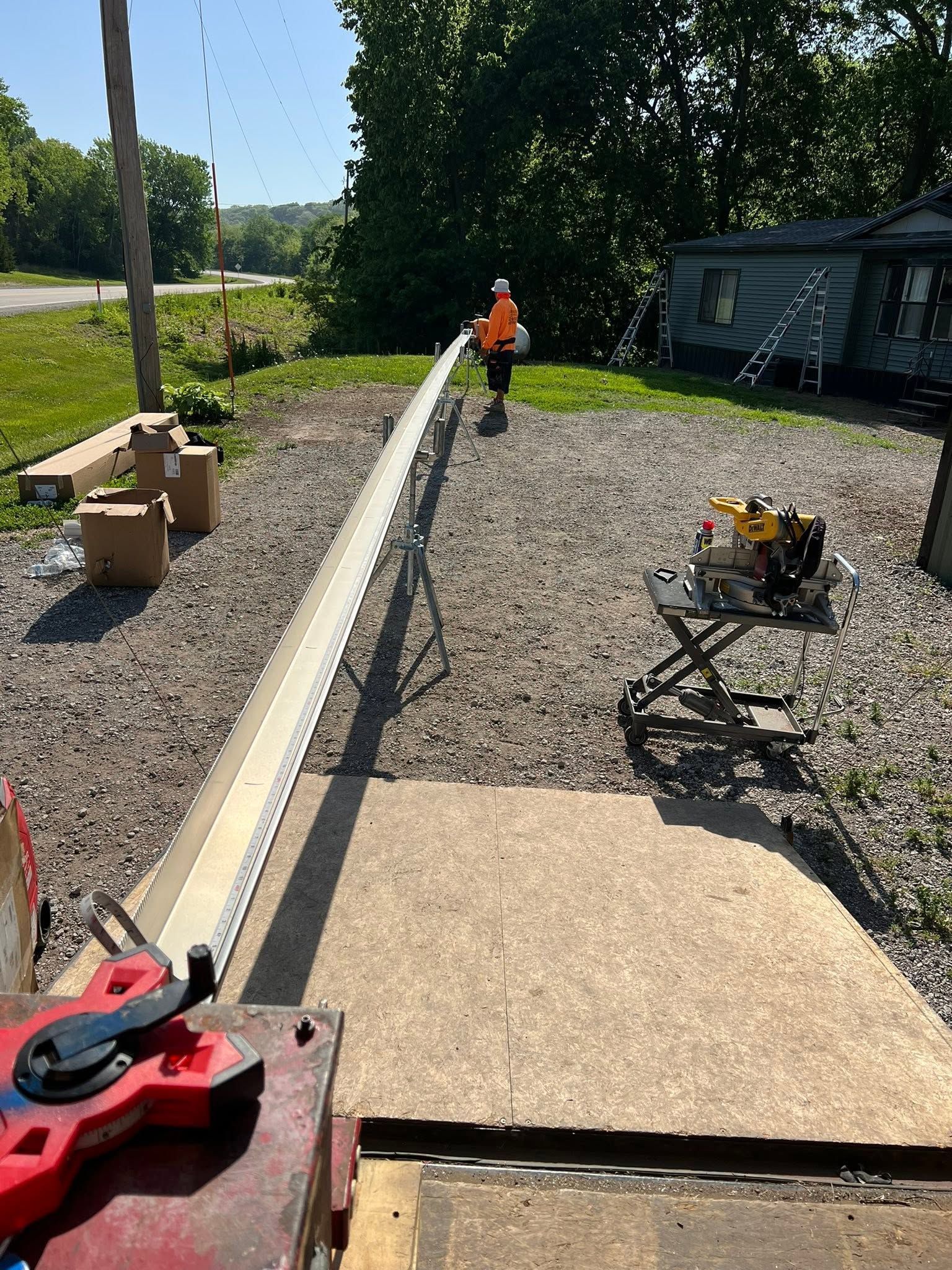 Worker in orange vest on gravel beside a long concrete edging at a construction site
