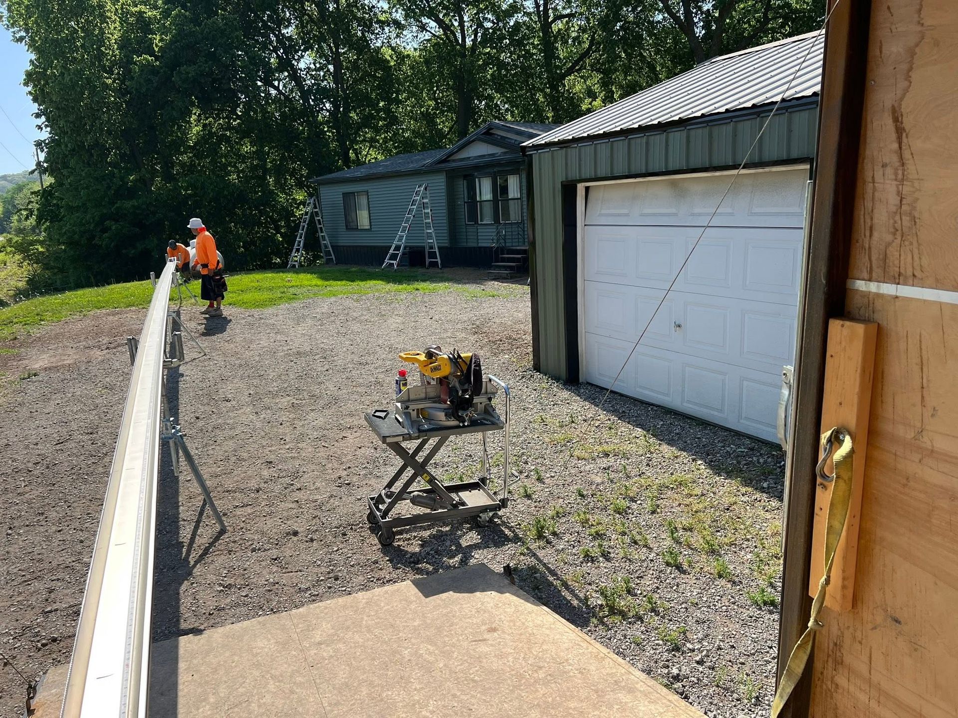 Construction worker on gravel beside a white garage, with a wheelbarrow and another building in the background