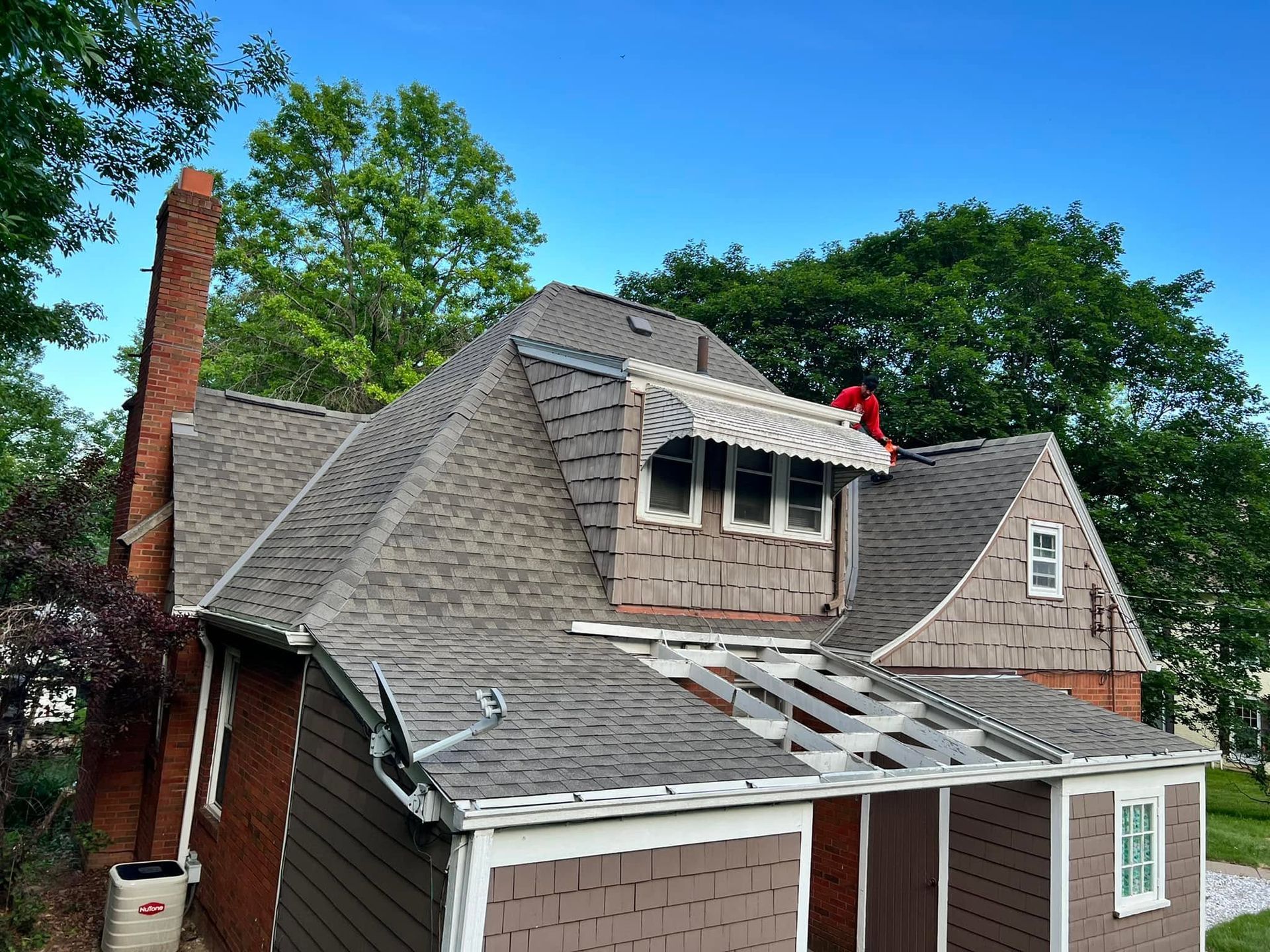 Roofers repairing a gray shingled house roof with a red chimney and dormer windows