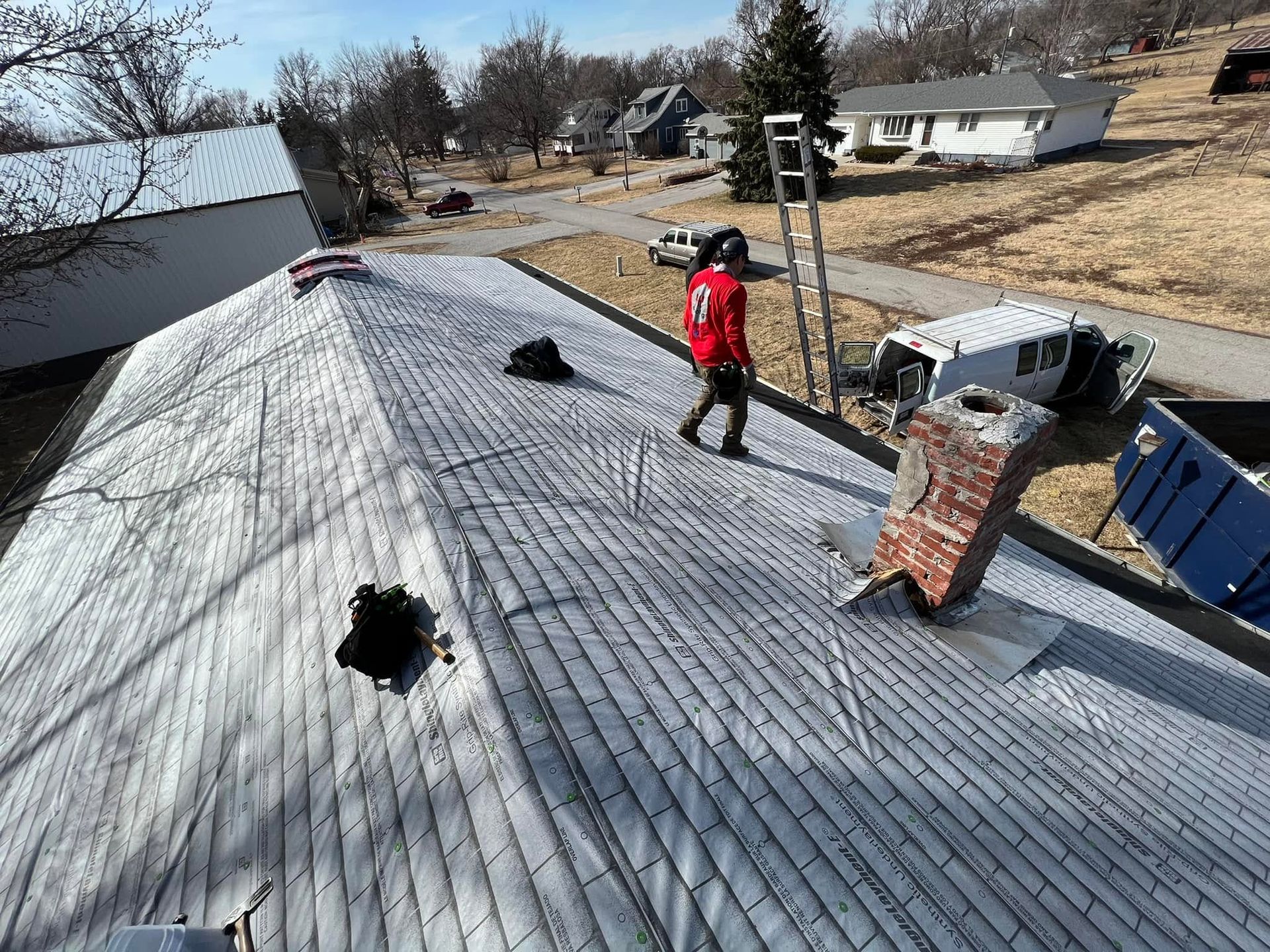 Worker inspecting a rooftop with several damaged sections and removed shingles.