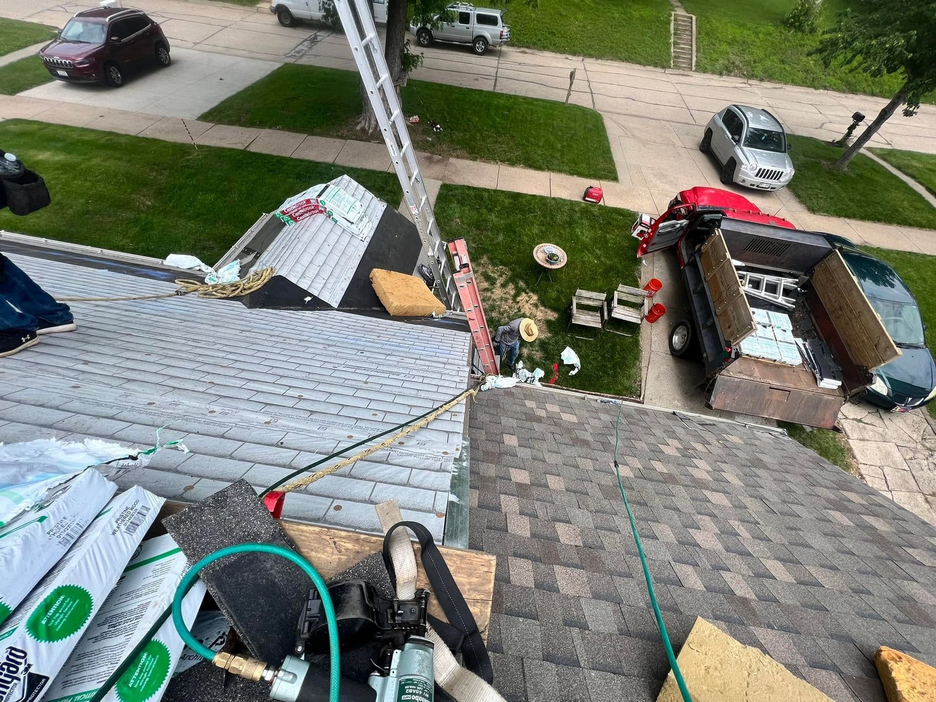 Roofer’s view of damaged shingles and exposed roof underlayment beside a ladder and debris below