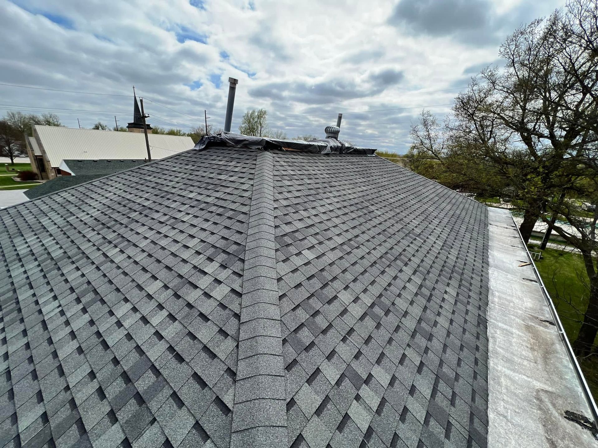 Gray shingled roof with a central ridge, seen from above under a cloudy sky.