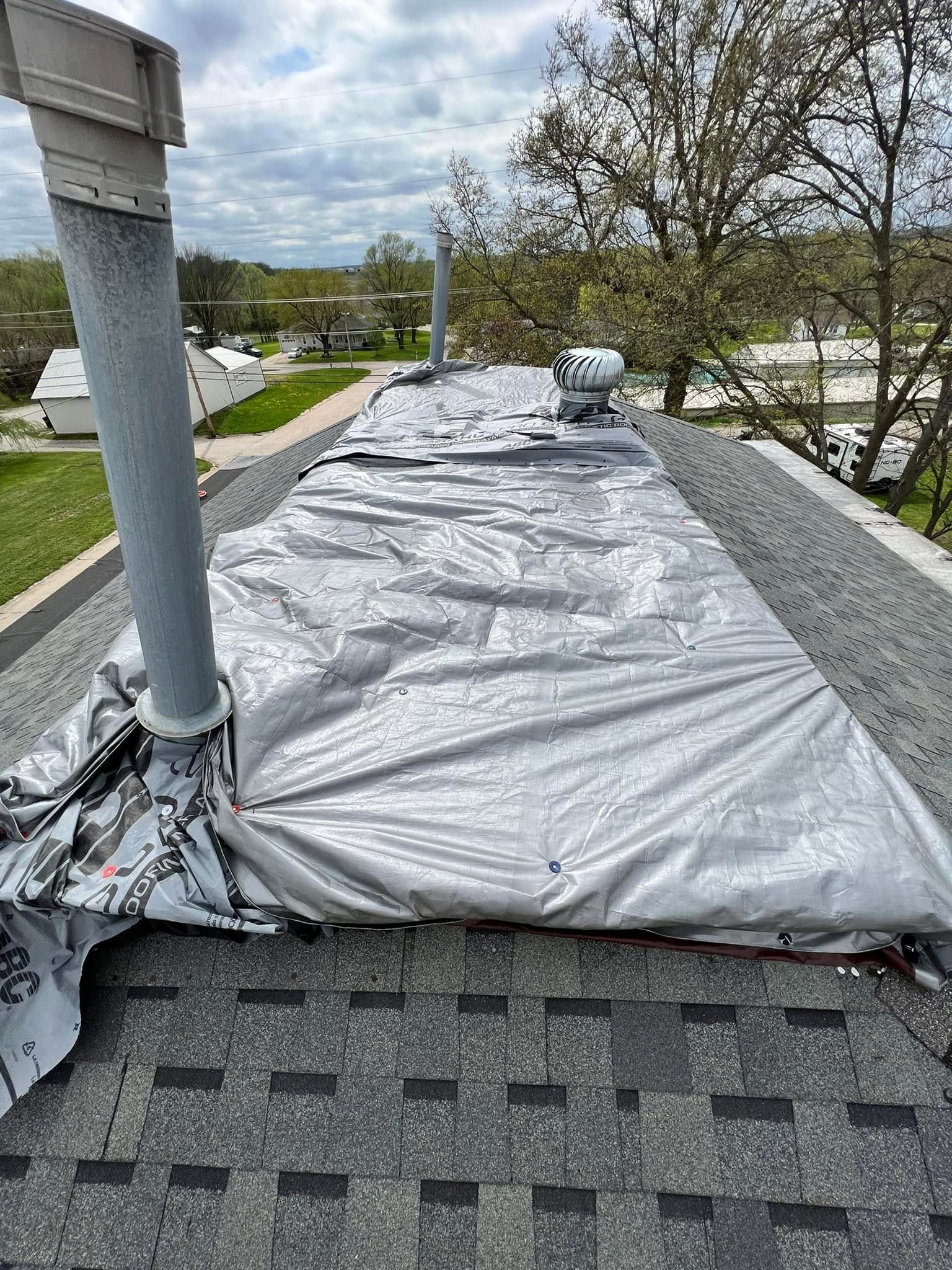 Rooftop with gray tarp covering a section, vent pipe, and cloudy sky in the background