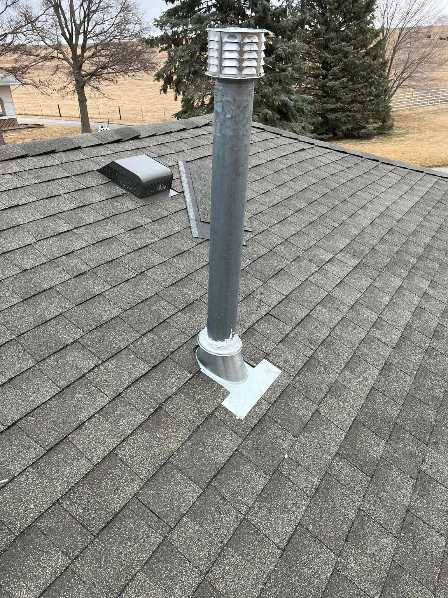 Rooftop vent pipe with cap on gray asphalt shingles, near a skylight.