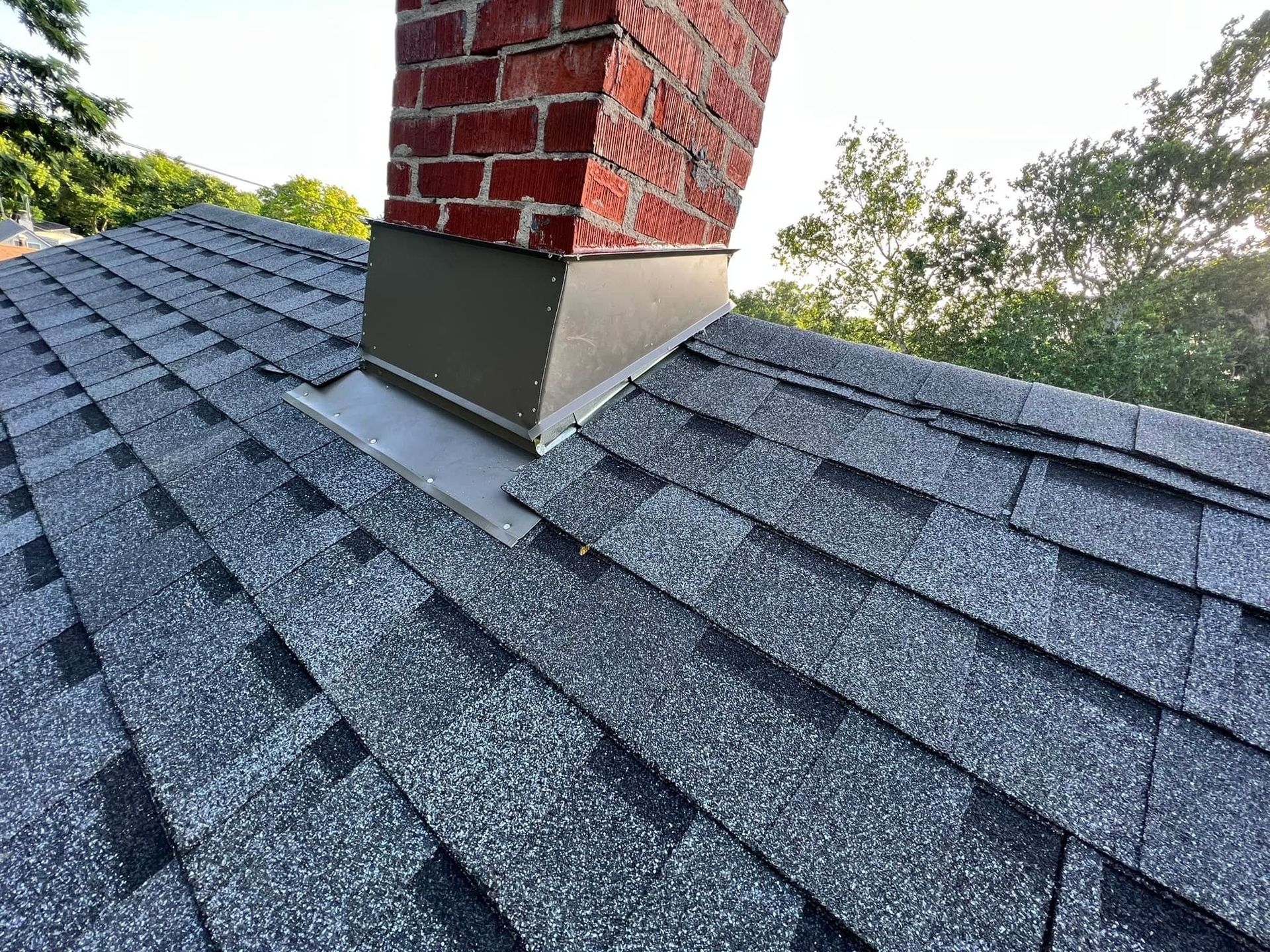 Damaged roof shingles around a brick chimney with exposed flashing and a slight roof dip