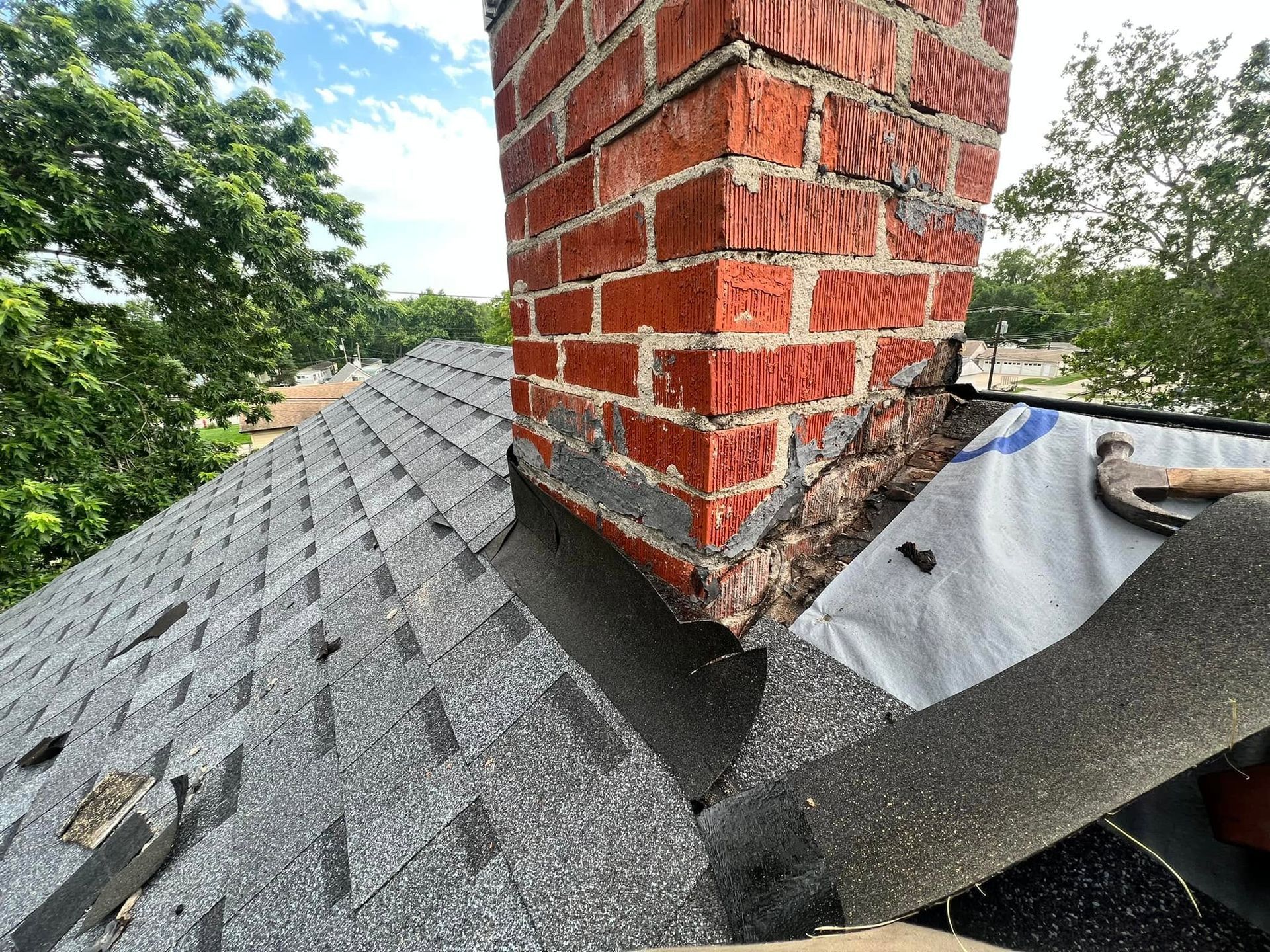 Roof valley around red brick chimney with gray shingles and flashing repairs under trees