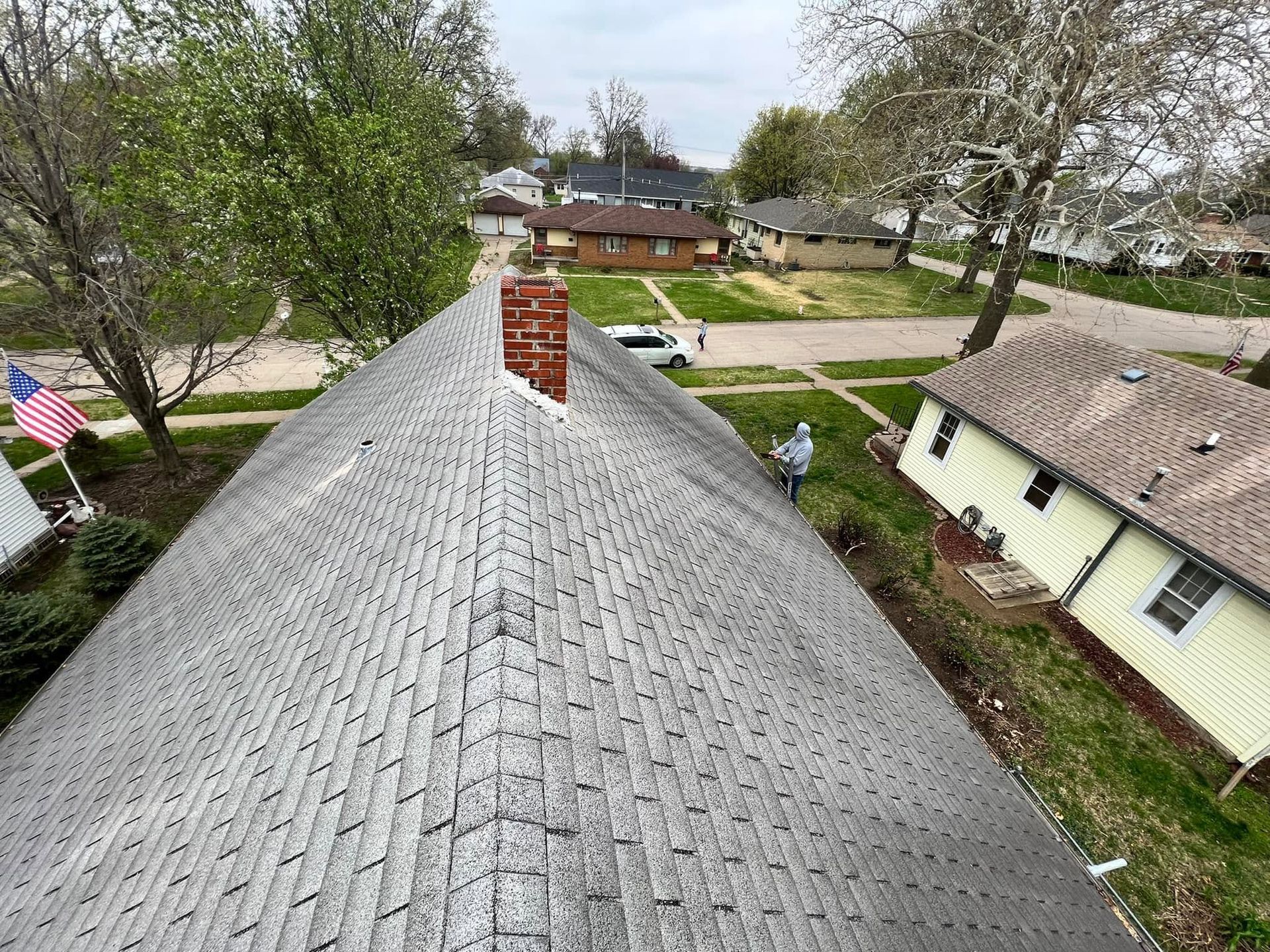 View from a roof over a suburban neighborhood with trees, houses, and an American flag.