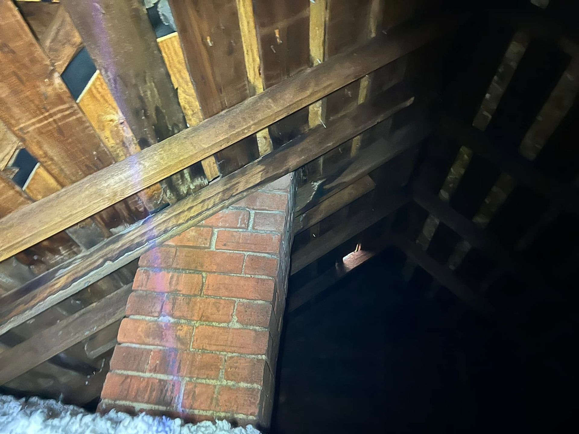 Attic with exposed wooden rafters and a brick chimney against a dark roof space