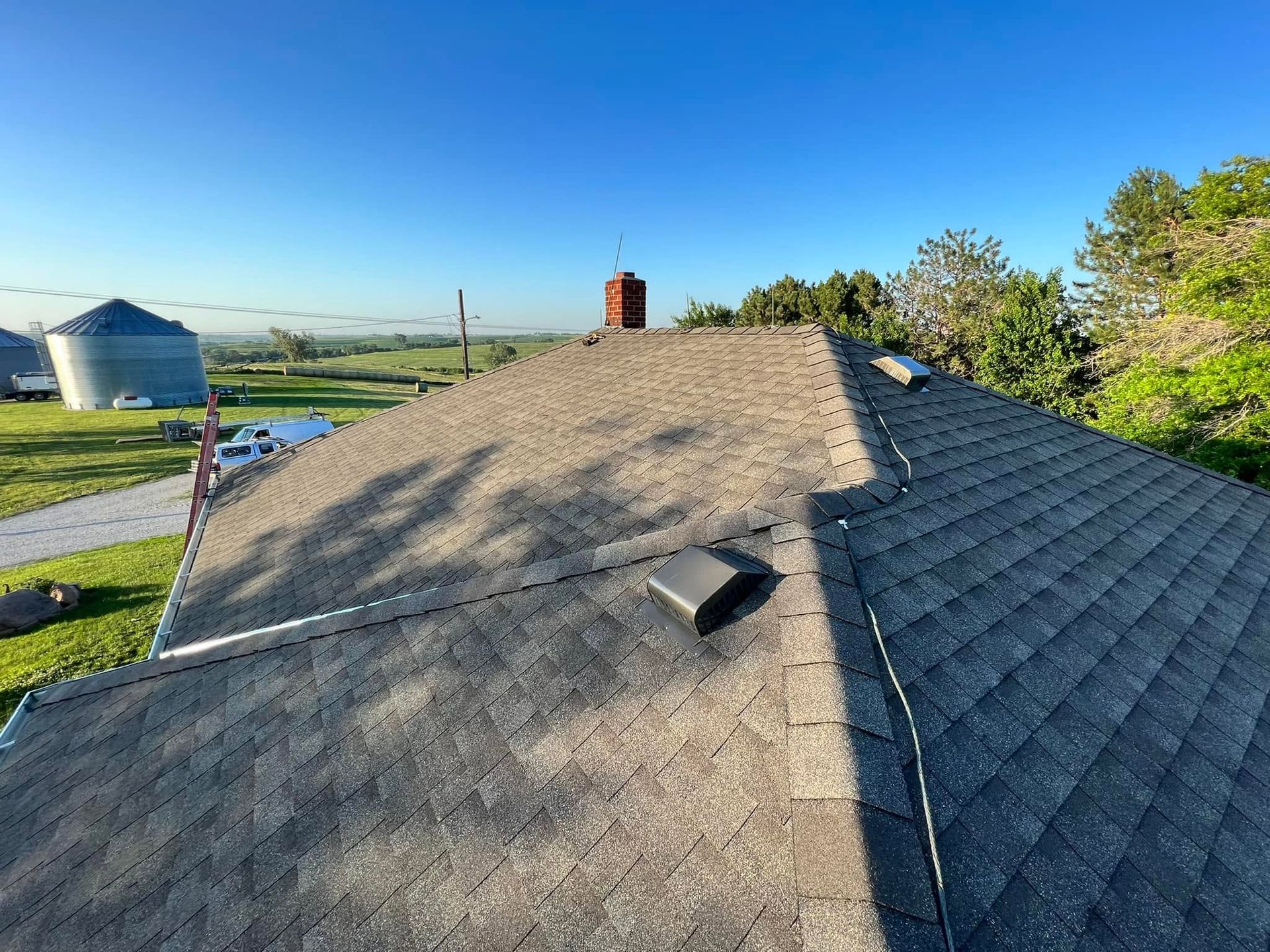 Rural rooftop with gray shingles, vent pipe, and a small skylight under a clear blue sky