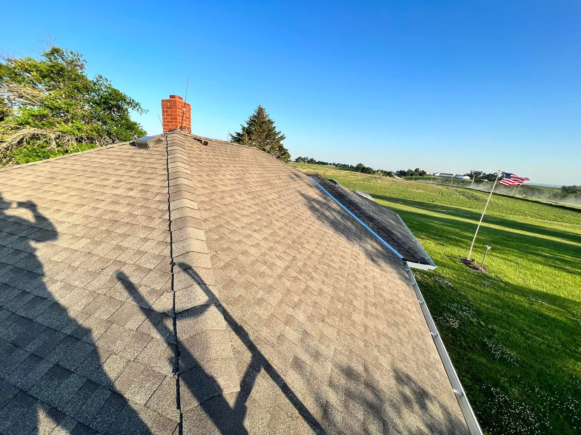 Thatched roof with chimney beside green fields under a clear blue sky