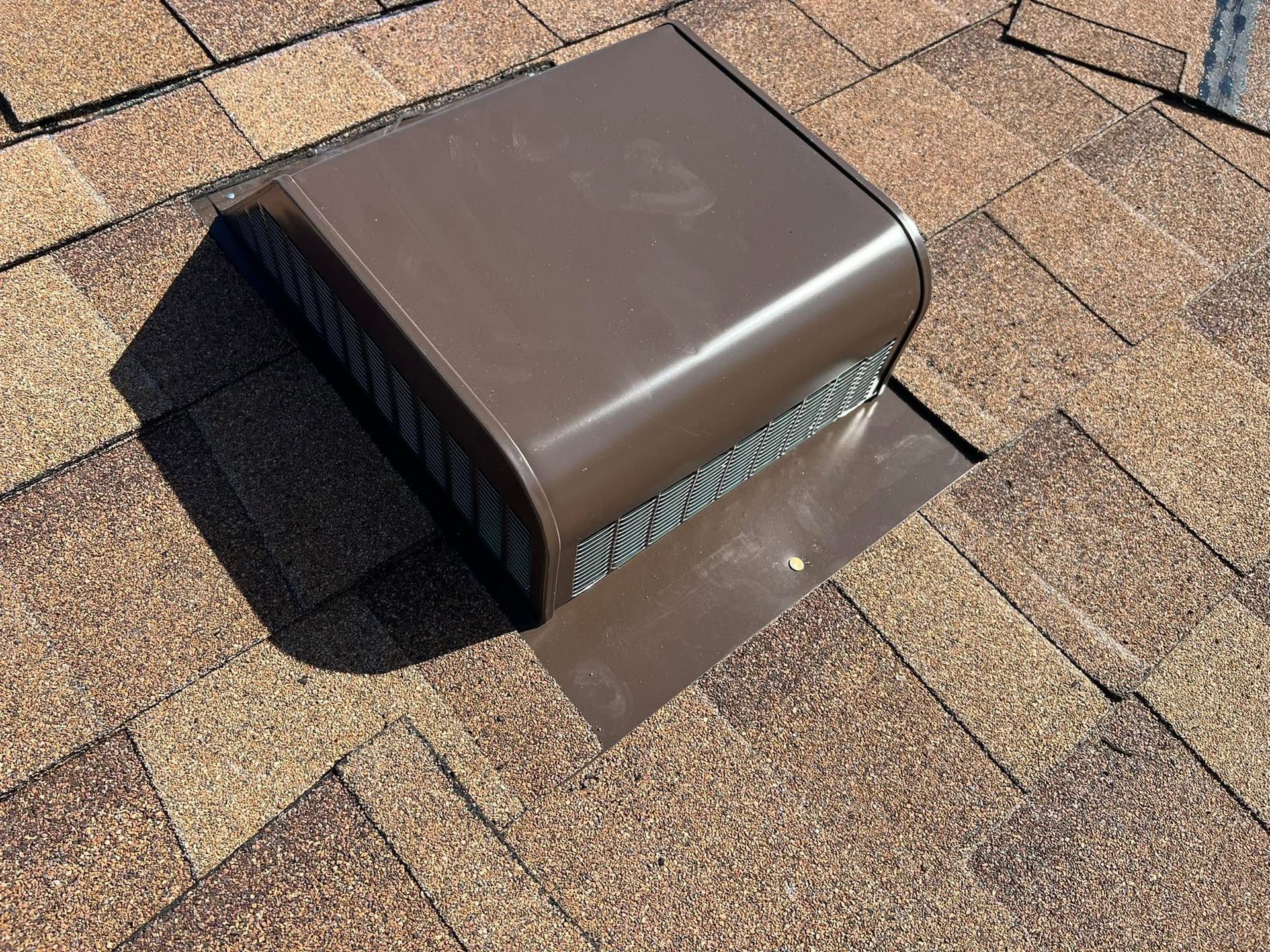 Brown roof vent protruding from asphalt shingles on a rooftop