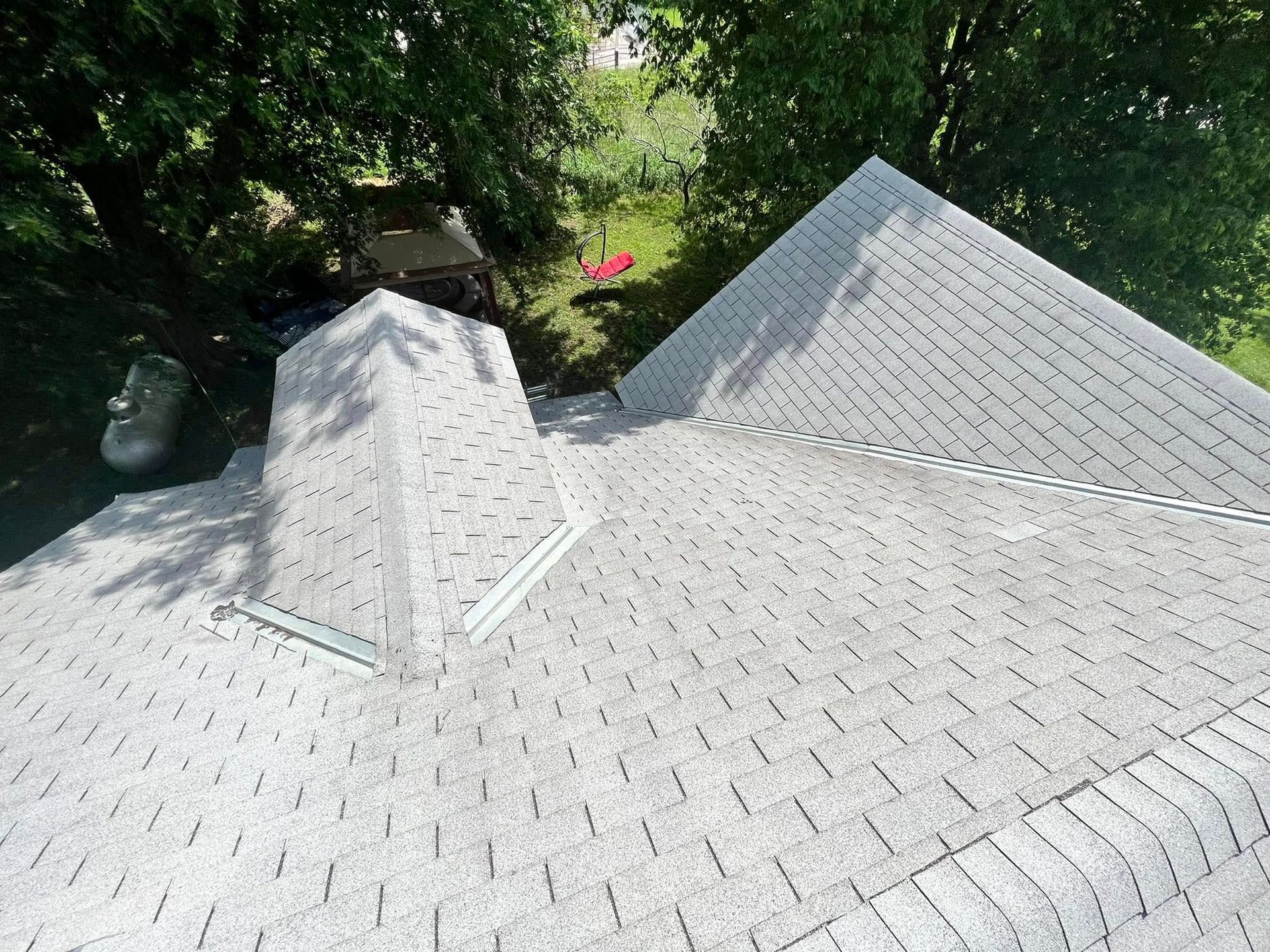 White shingled roof with two dormers, viewed from above beside green trees and a red umbrella in the yard
